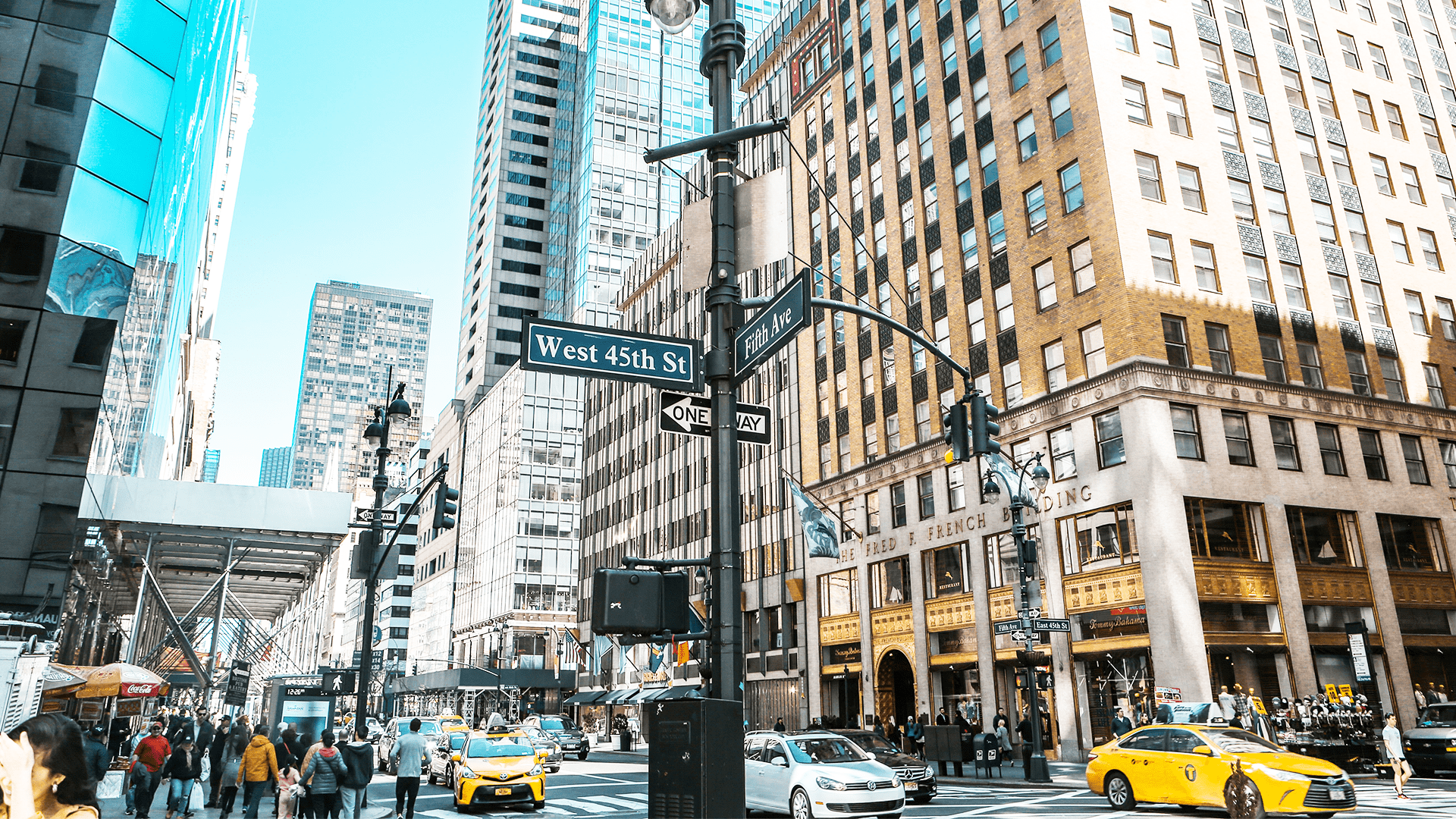 Gatekryss ved Fifth Avenue og West 45th Street i New York City med høye bygninger, travle fotgjengere og gule taxier i forgrunnen.