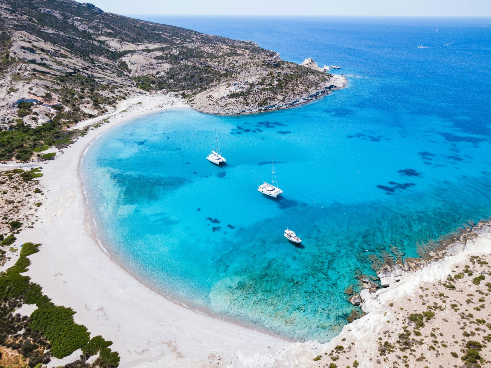 Blå havstrand og båter på kysten av Milos