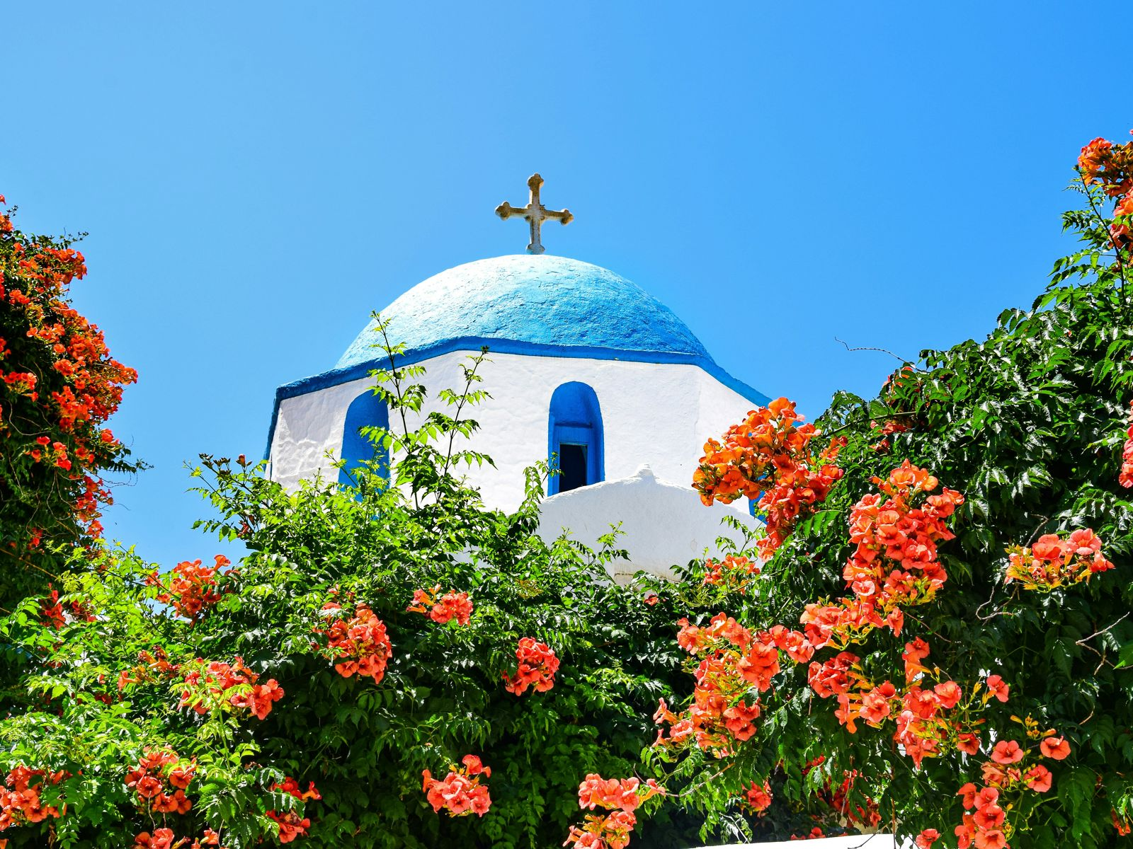 Gresk kirketårn med blått tak omgitt av grøntområder og vakre blomster