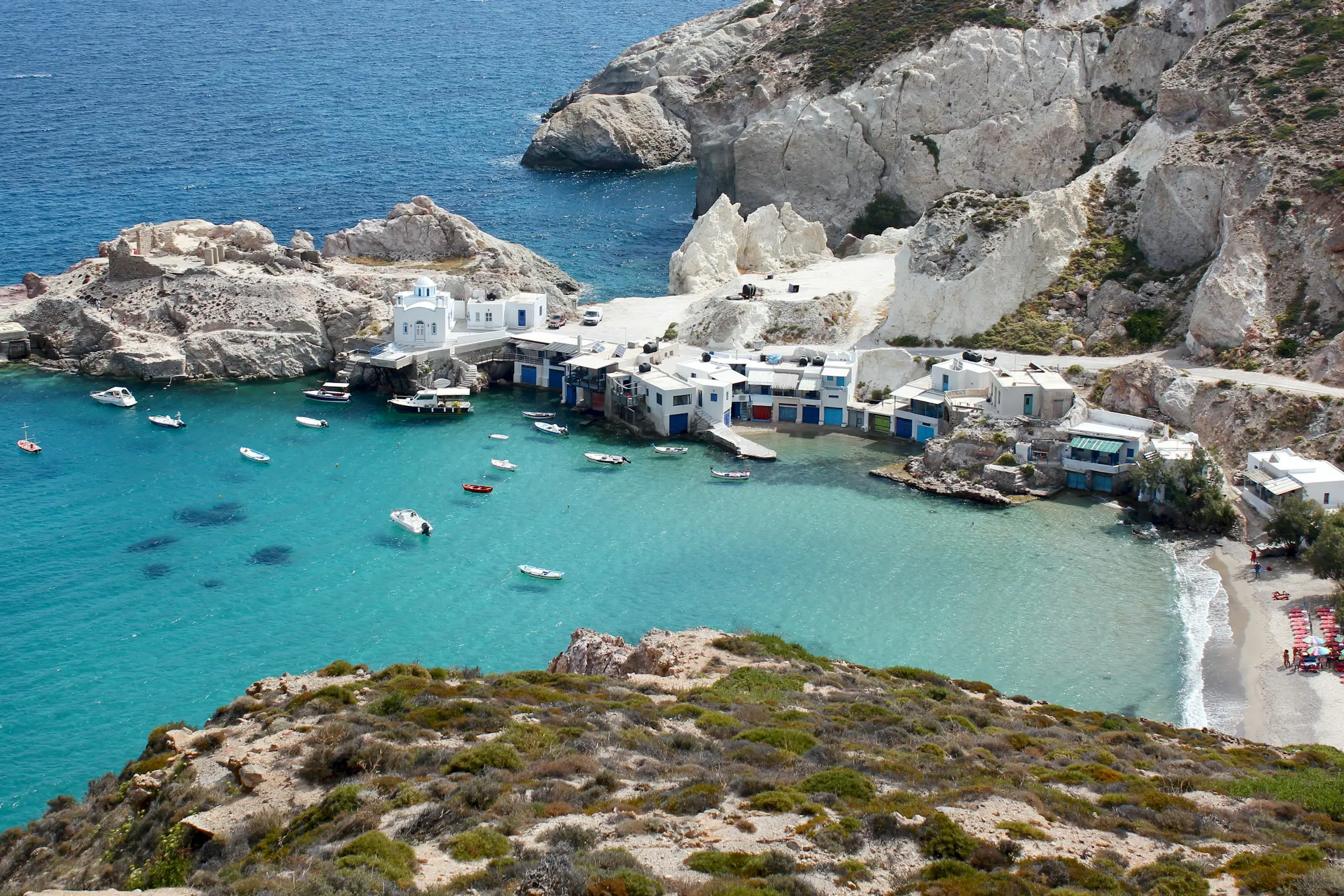 Kystlandskap på Milos, Hellas med tradisjonelle hvite hus og båter ved asurblått hav.