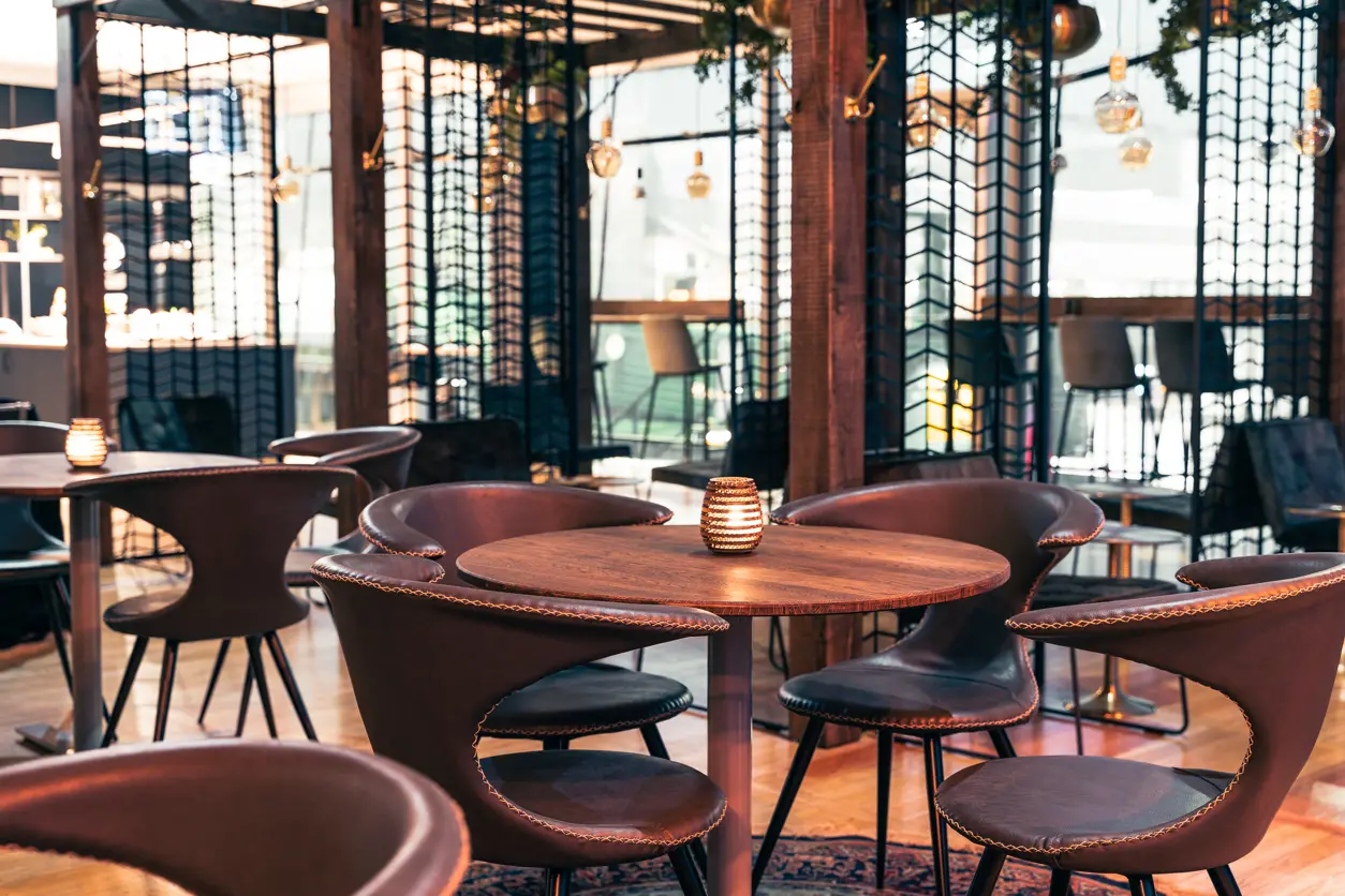 Loungeområde med runda träbord och mörka stoppade stolar, mjuk belysning och dekorativa lampor i en modern inomhusmiljö.