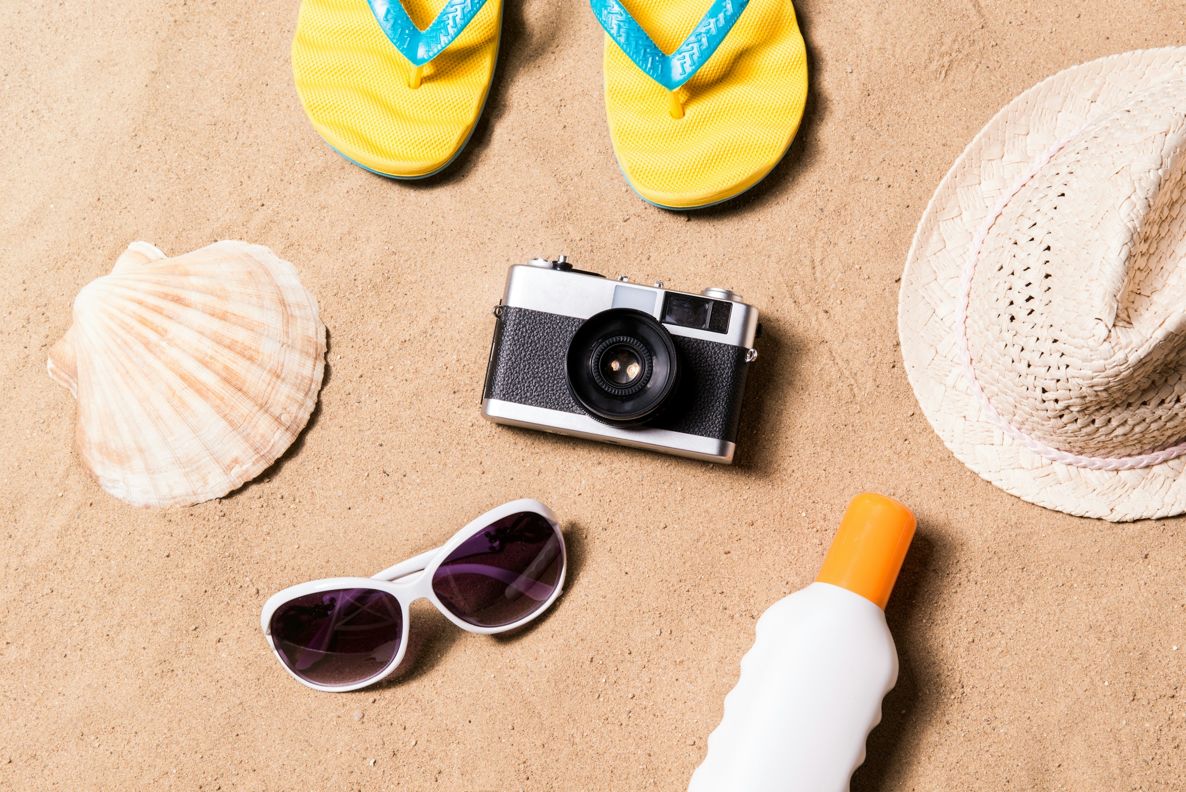 Reiseprodukter som lue, kamera og solkrem på en sandstrand