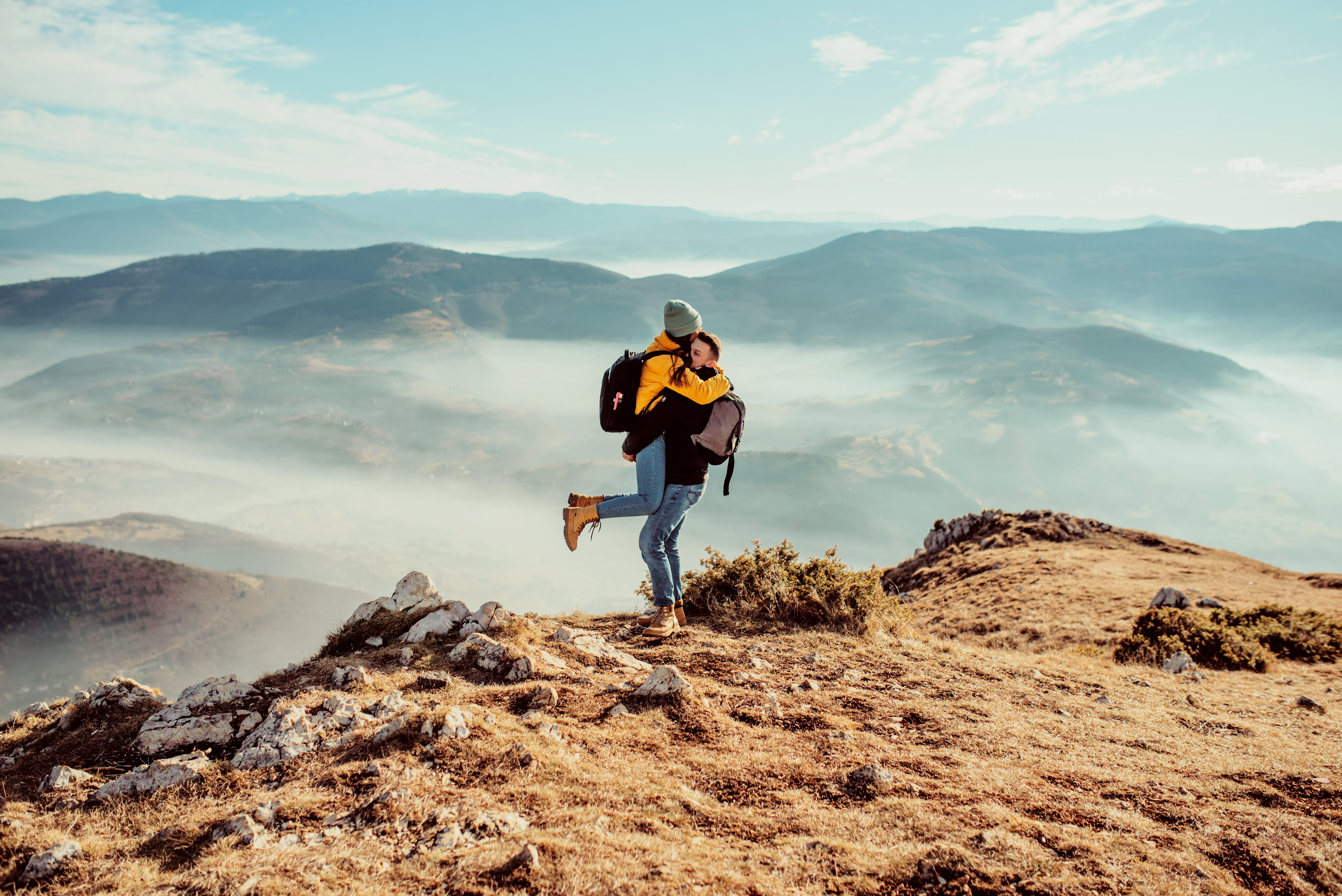 Couples are insured on the trip and hug on a mountain top with misty valleys in the background.