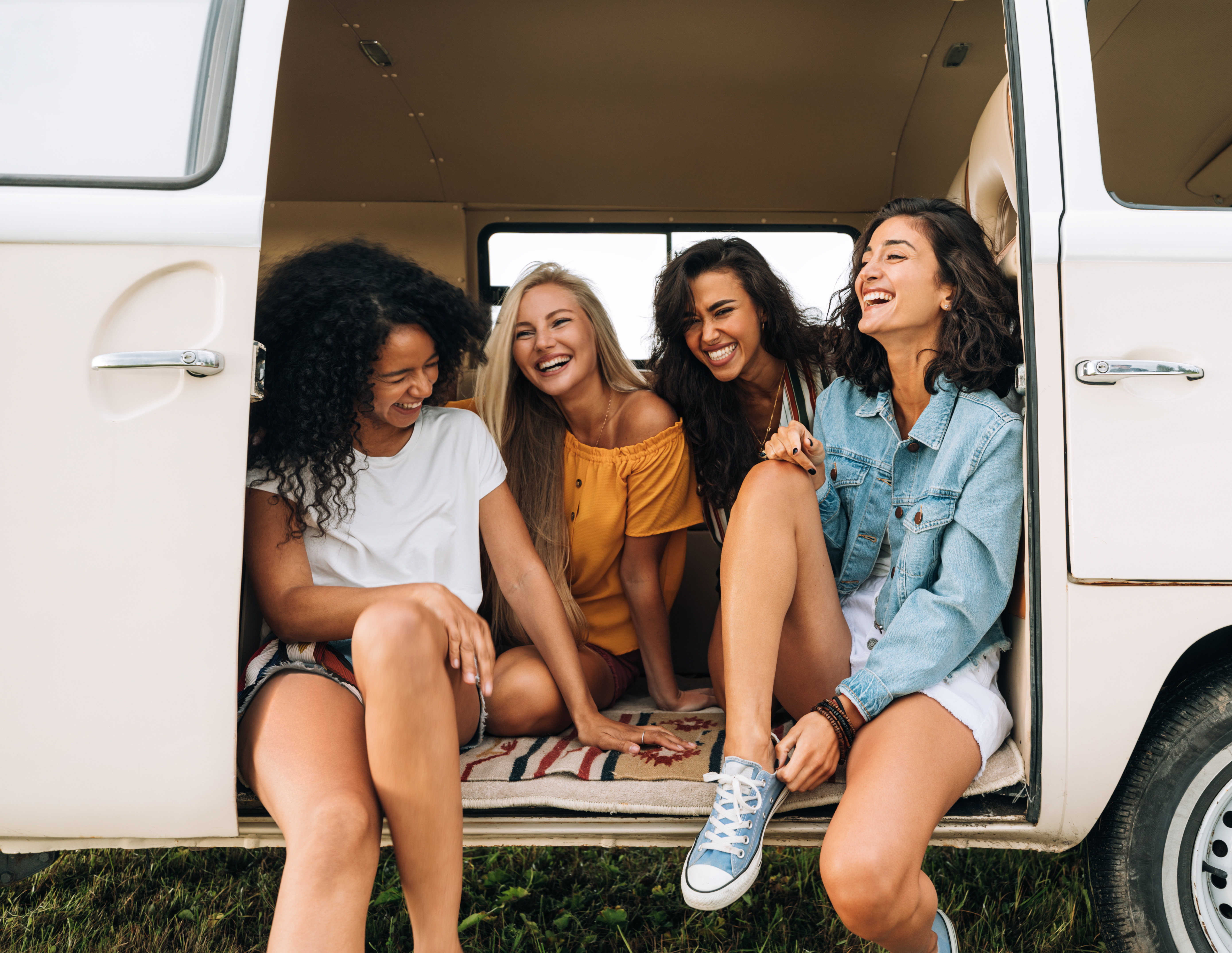 Travel insurance for the trip - Happy young women sitting and laughing in a van during a summer day, friendship and road trip concept.