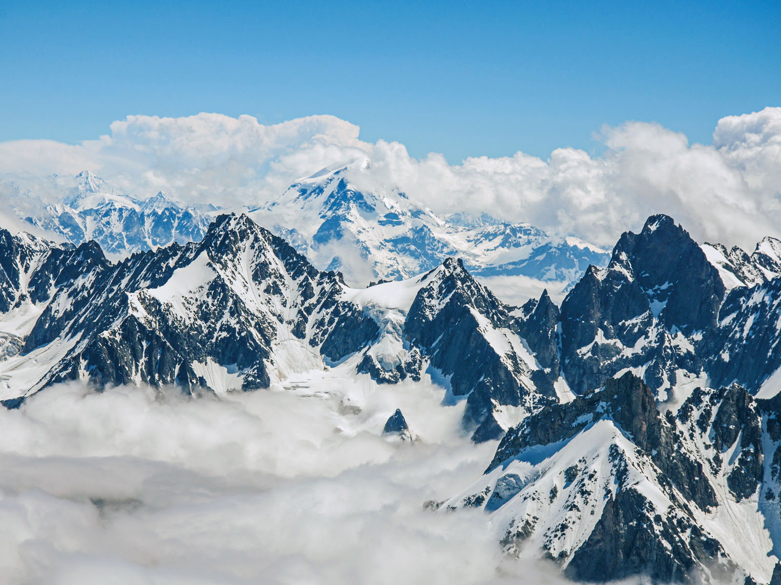 Høye snødekte fjell i Alpene med blå himmel i bakgrunnen