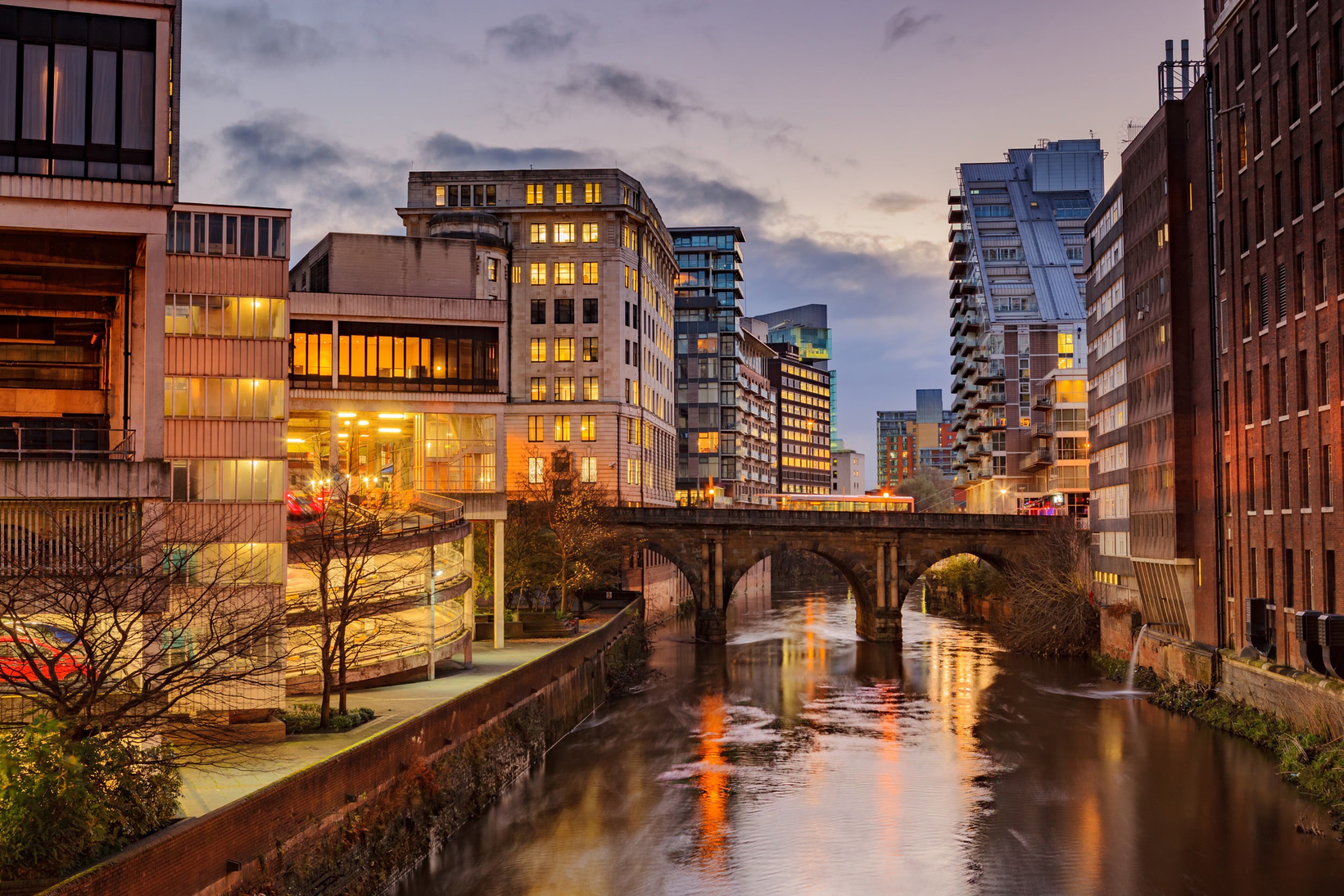 Houses and skyscrapers like shining windows following a river during the evening in Manchster