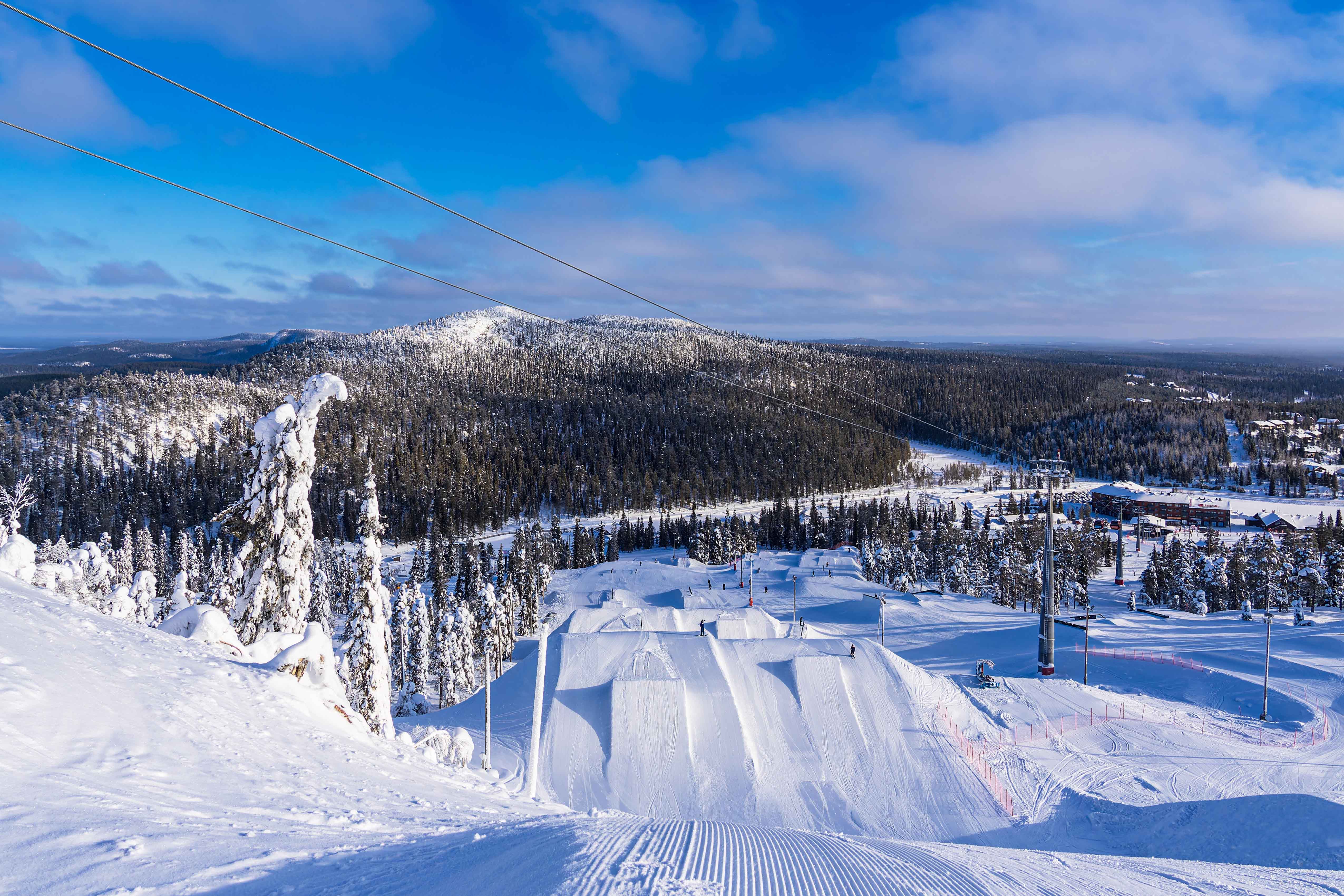 Travel to Ruka - Snow-covered ski slope leads down to dense forest and snow with blue sky in the background in Finland