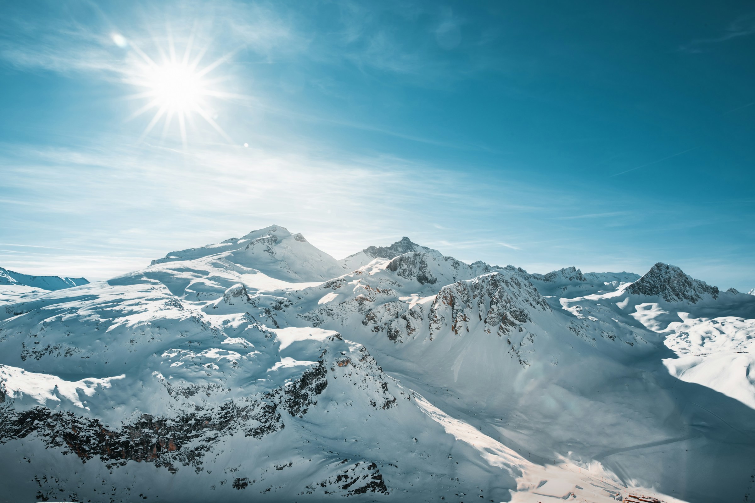 Sunlight beaming over snow-capped mountain peaks against a clear blue sky in Val d'Isére, France.