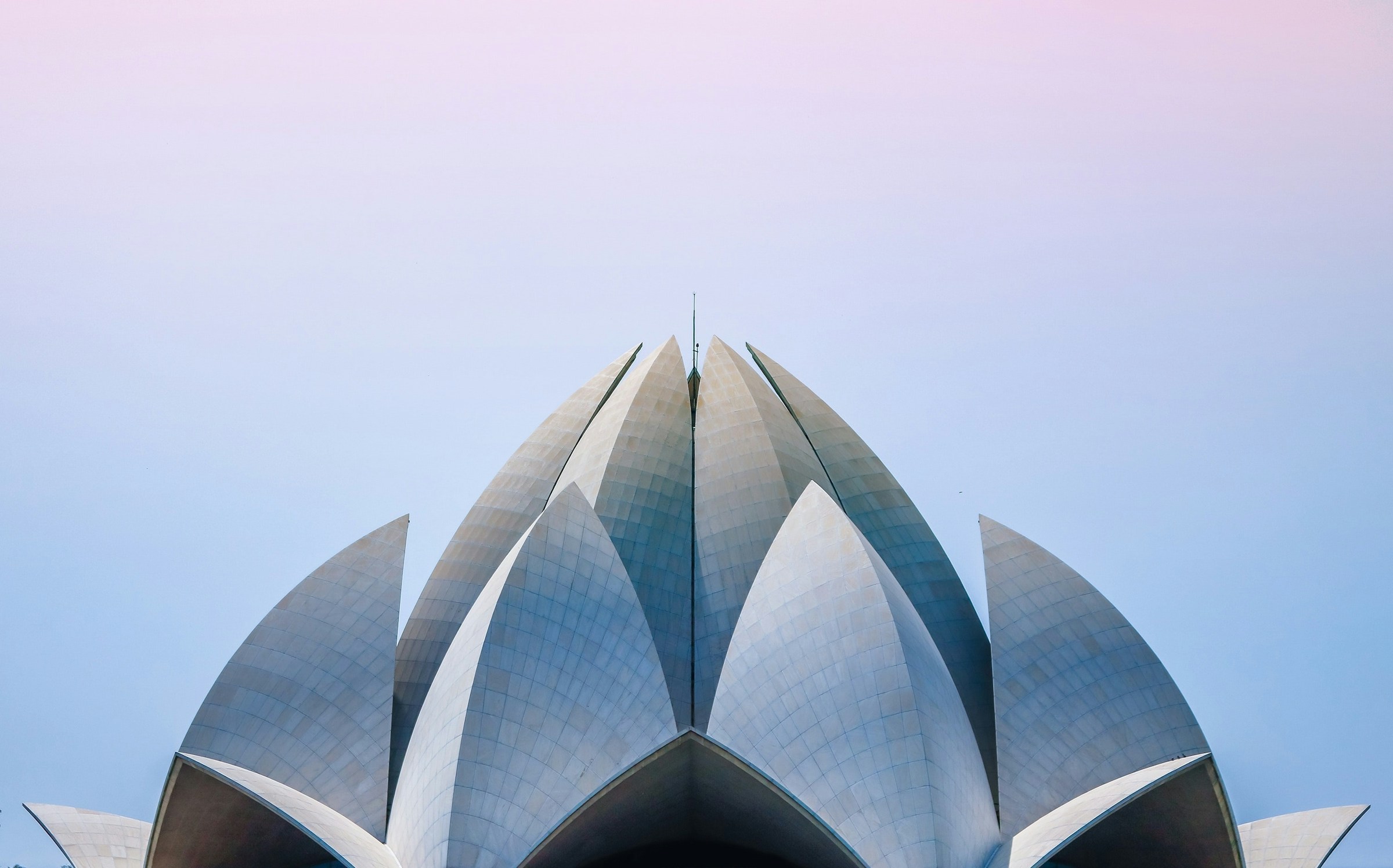 Symmetrisk utsikt over en moderne bygning med lotuslignende struktur mot en pastellfarget himmel i Delhi.