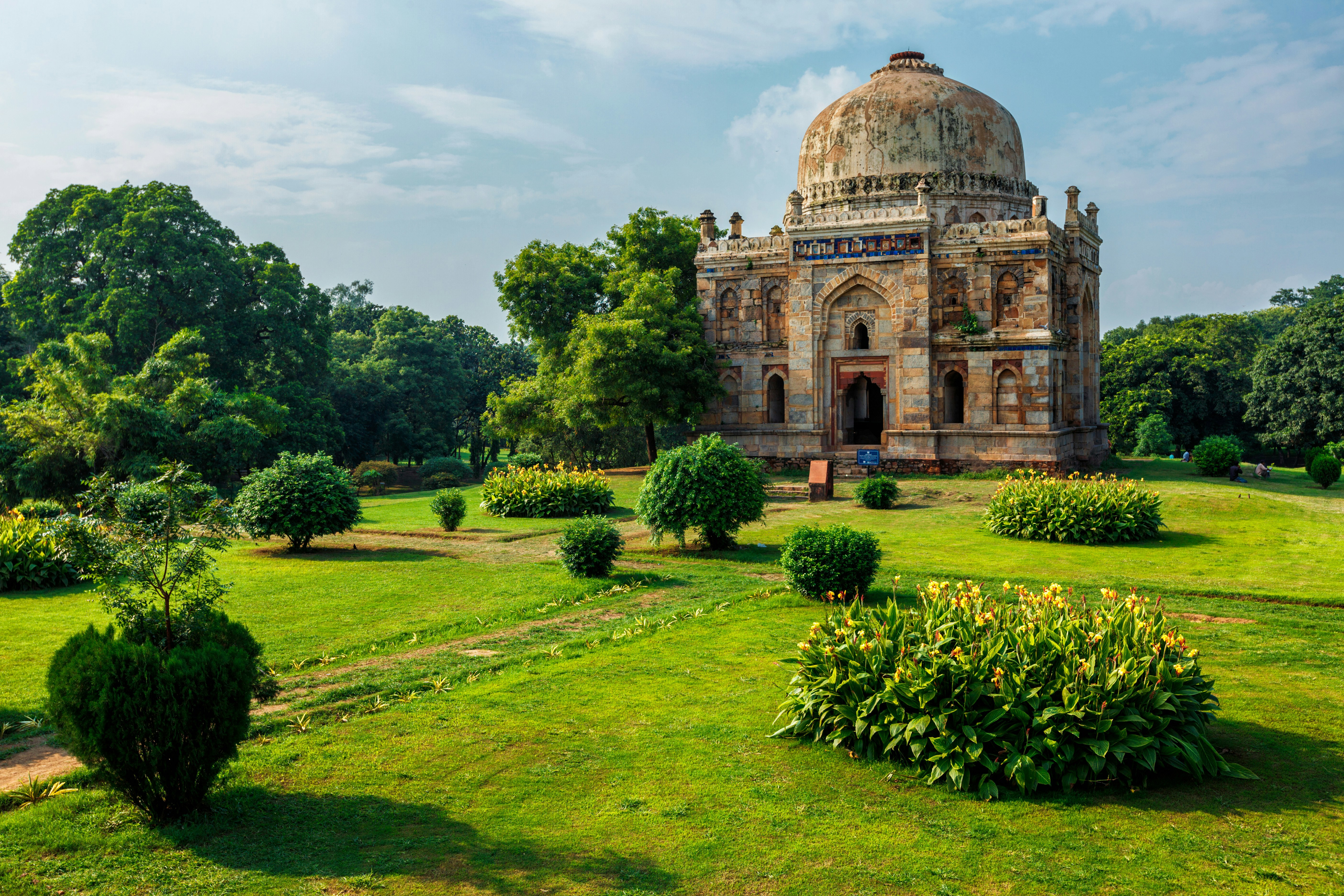 Frodig hage og historisk kuppelformet bygning under klar blå himmel i Delhi.