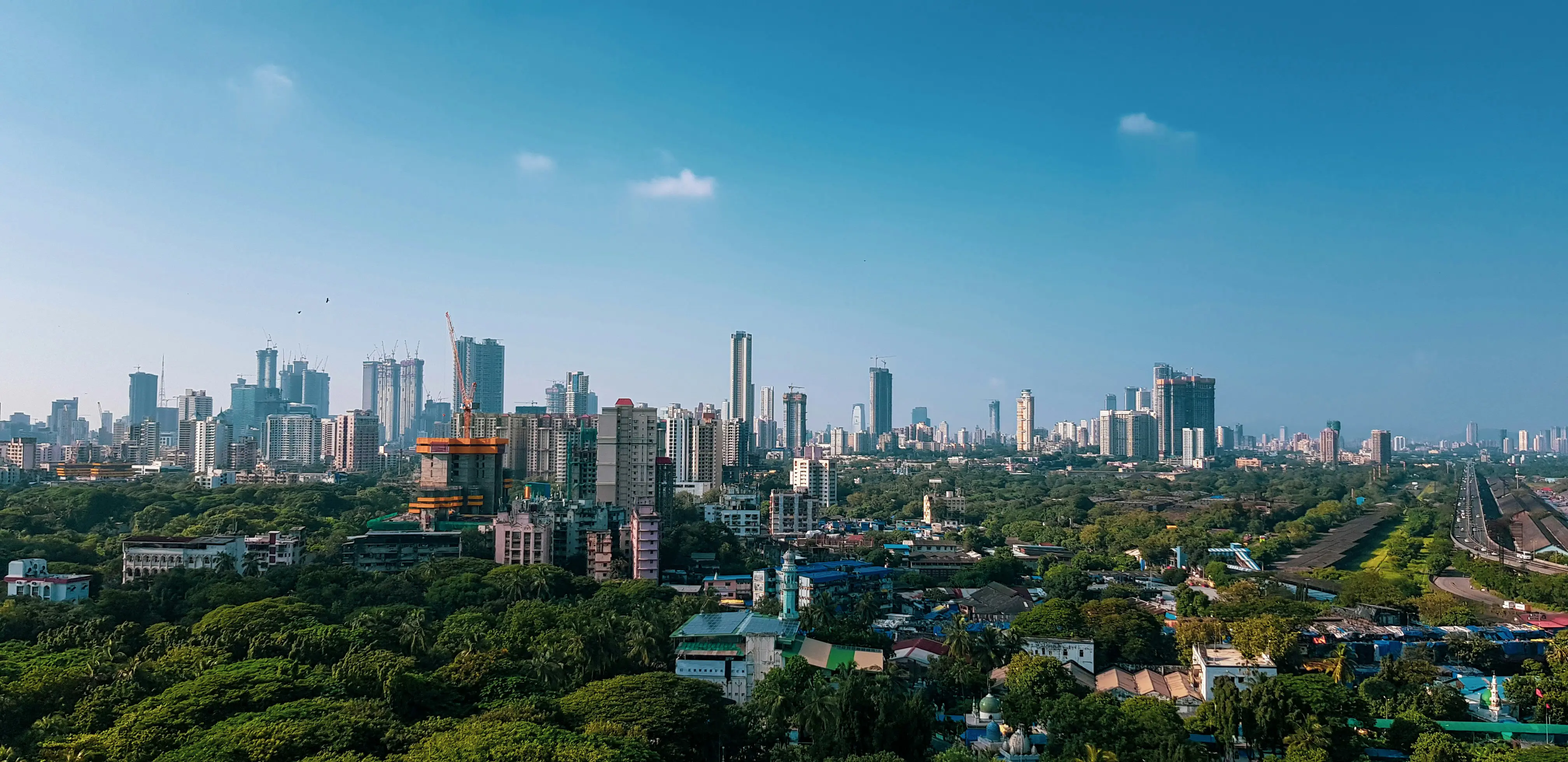 Reis til Mumbai - Panoramautsikt over Mumbai med skyskrapere, grønne parkområder og en klar blå himmel.