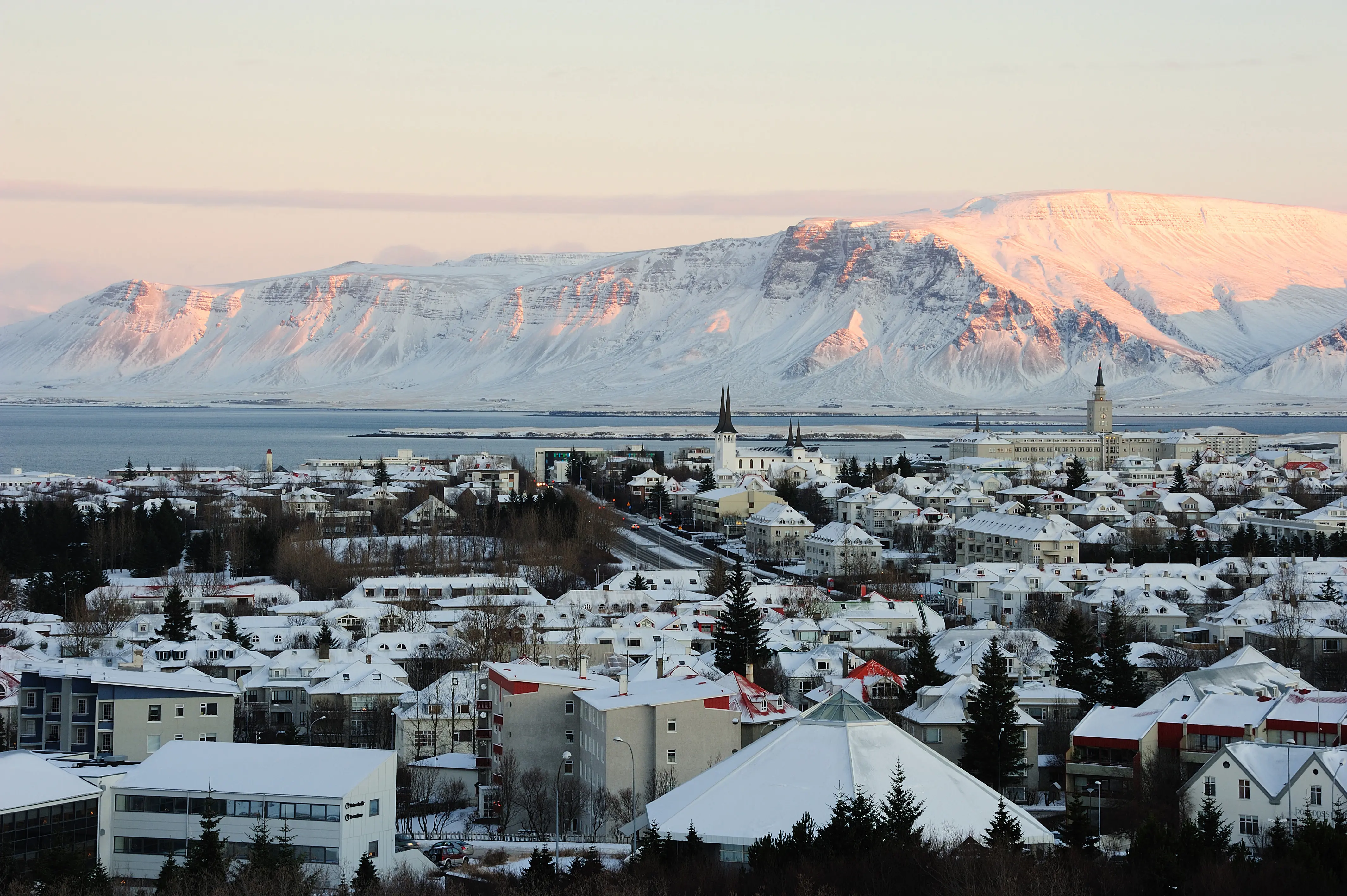 Utsikt over Reykjavik by med fjell i bakgrunnen under en solnedgang