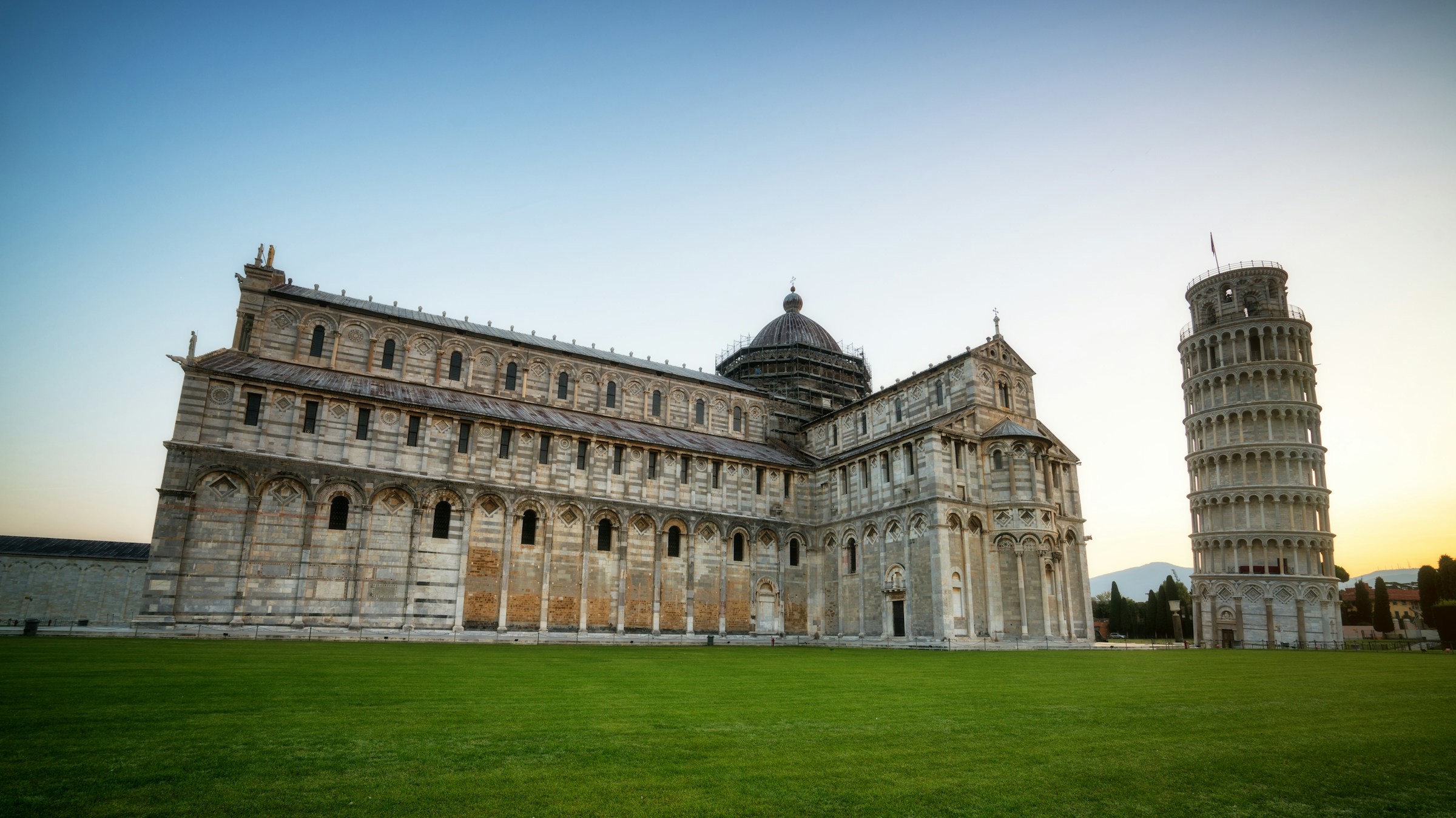 Vakker tradisjonell italiensk hvit bygning på en plen med skjevt tårn i Pisa ved siden av