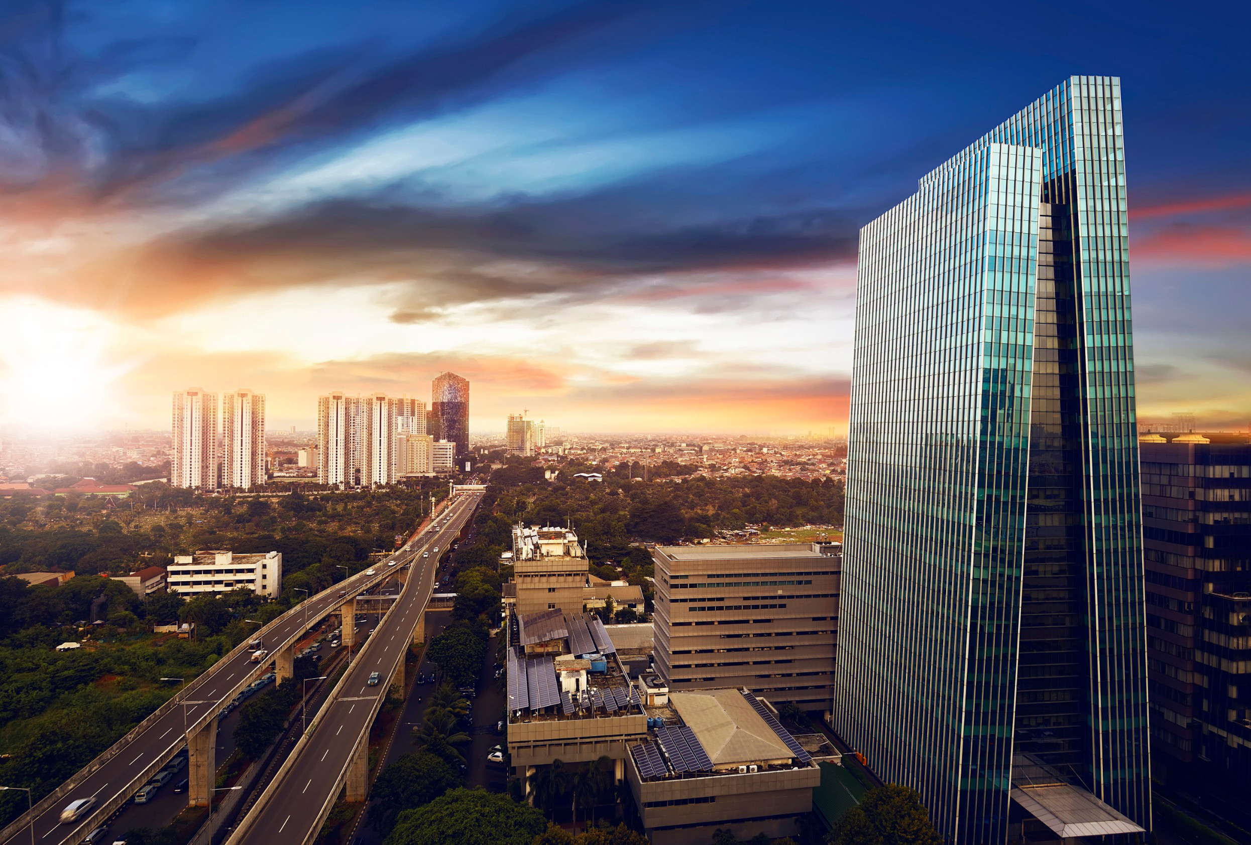 Solnedgang over Jakarta by med motorvei og glassskyskraper med bysilhuett i bakgrunnen