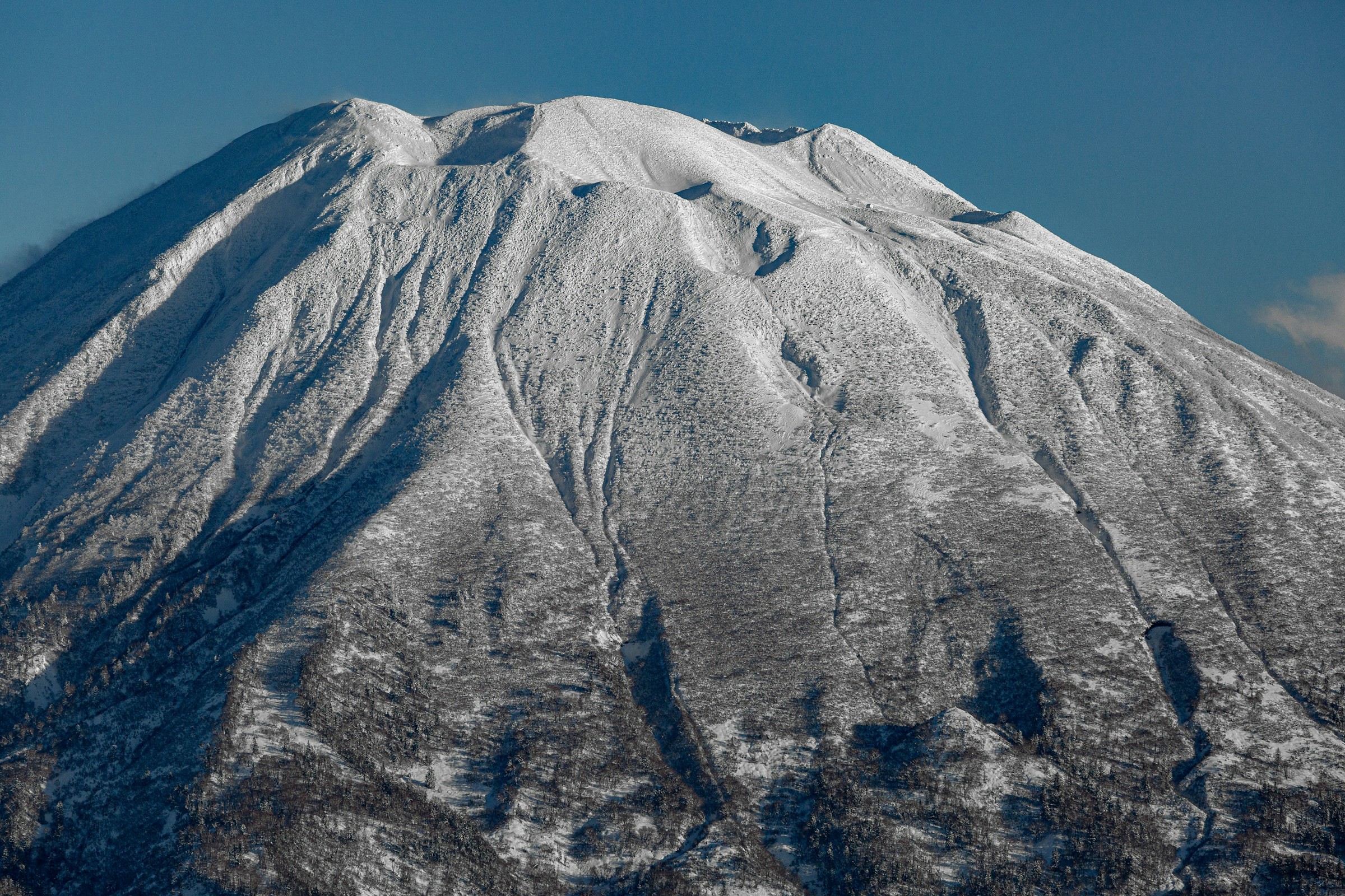 Snow-capped mountain peak under clear blue sky, dramatic shadows over the mountainside.