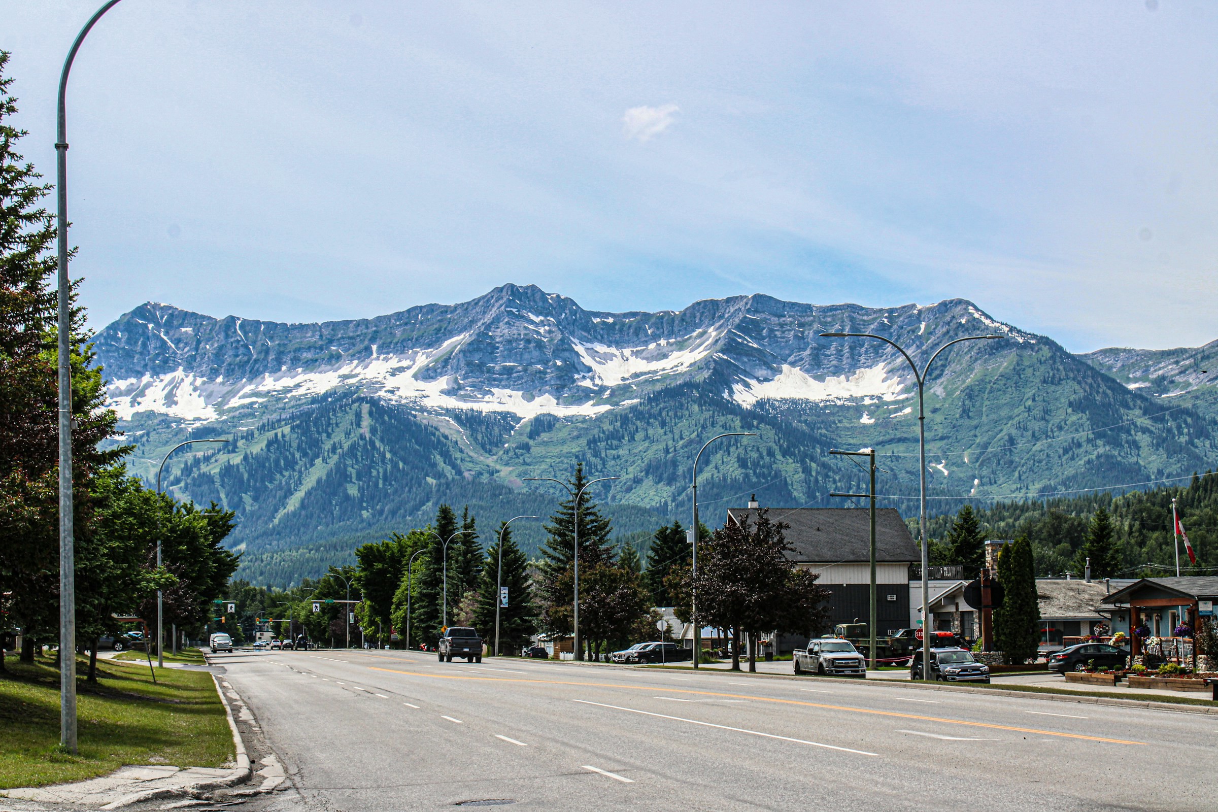 City street with views of snow-capped mountain peaks and green slopes under a clear blue sky in Fernie, Canada.