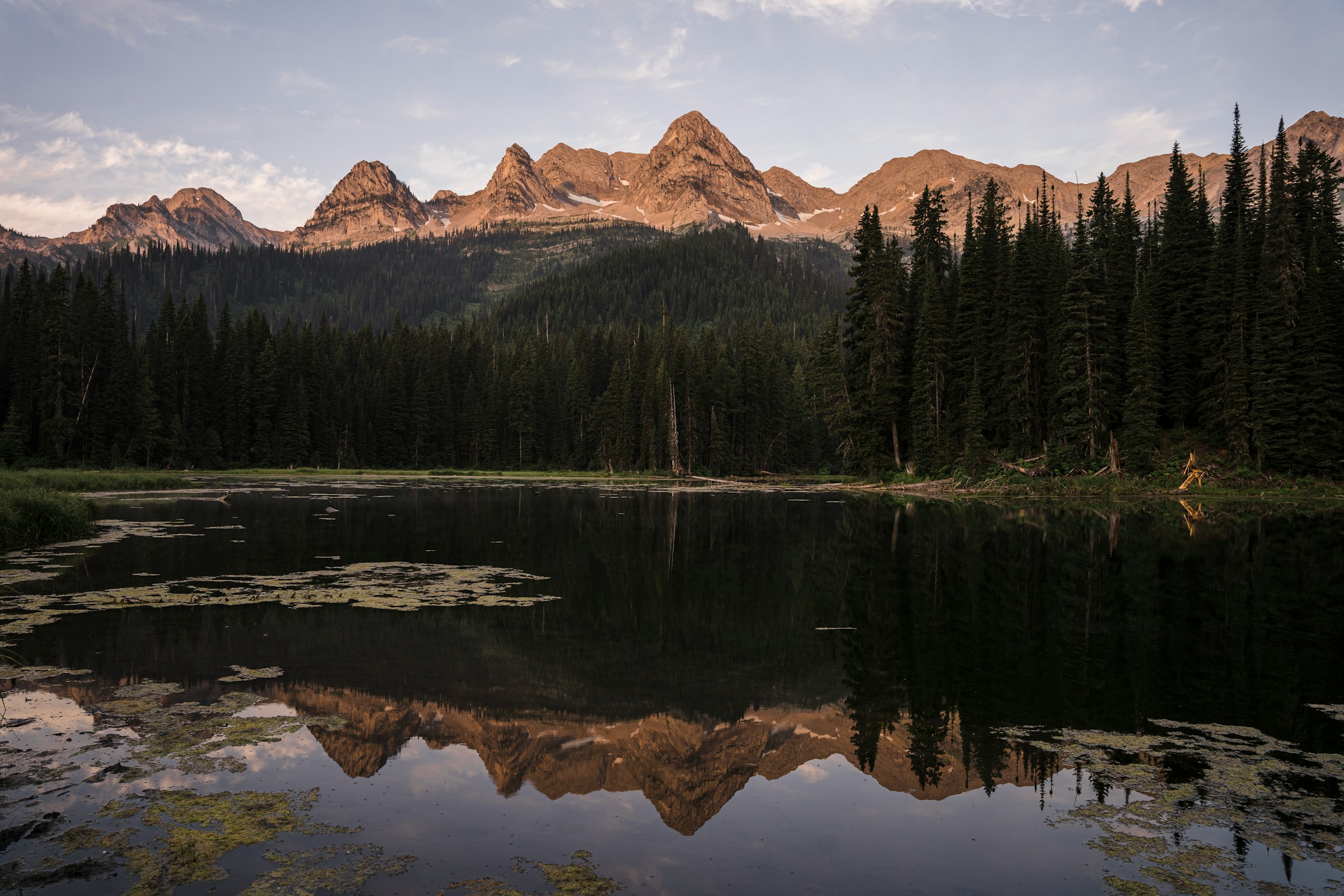 Trip to Fernie - Mountain reflection in a tranquil forest lake at sunset and a mountain range in the background.