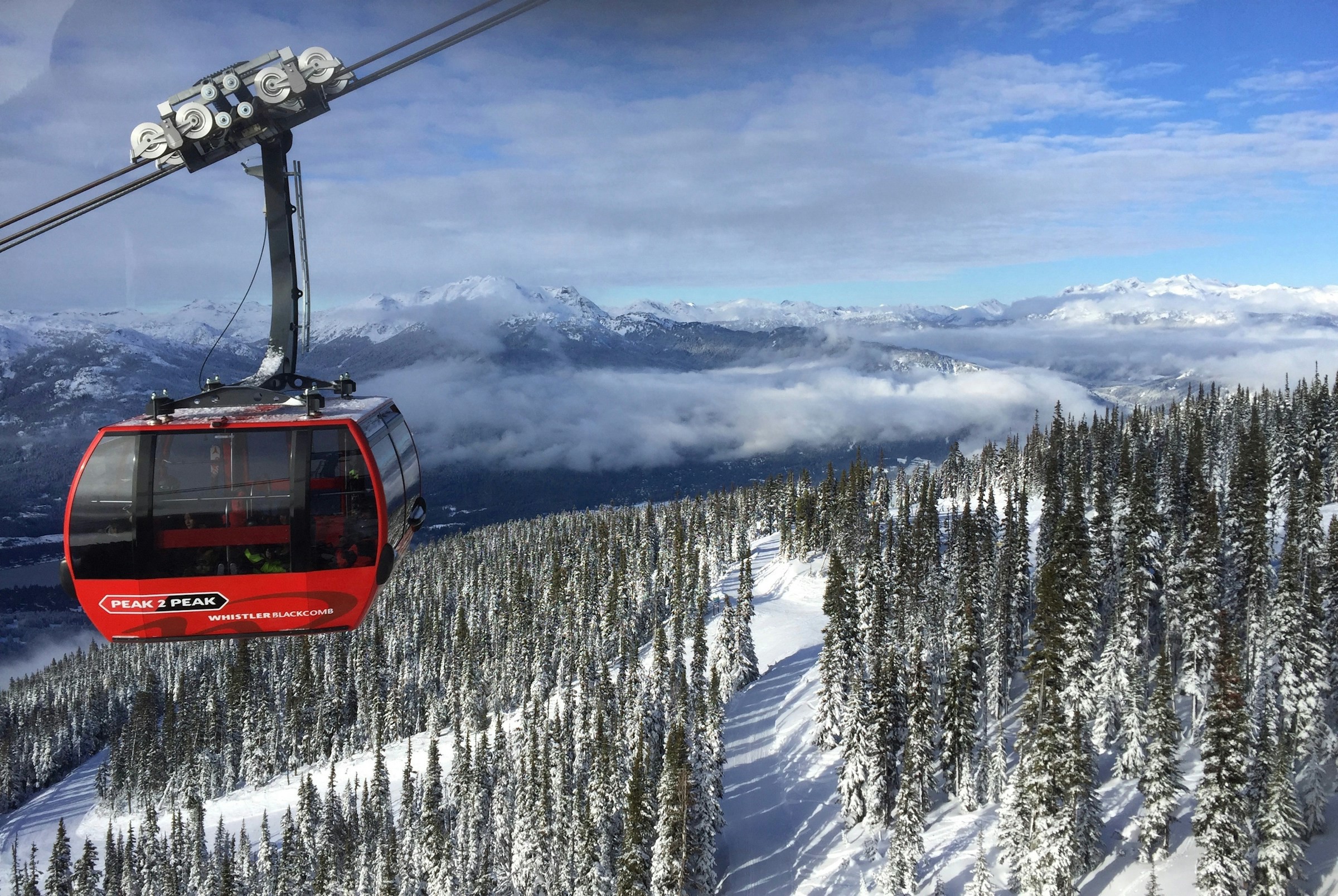 Red gondola lift against the backdrop of snow-capped mountains and forests in Whistler Blackcomb, perfect for skiing and mountain tourism.