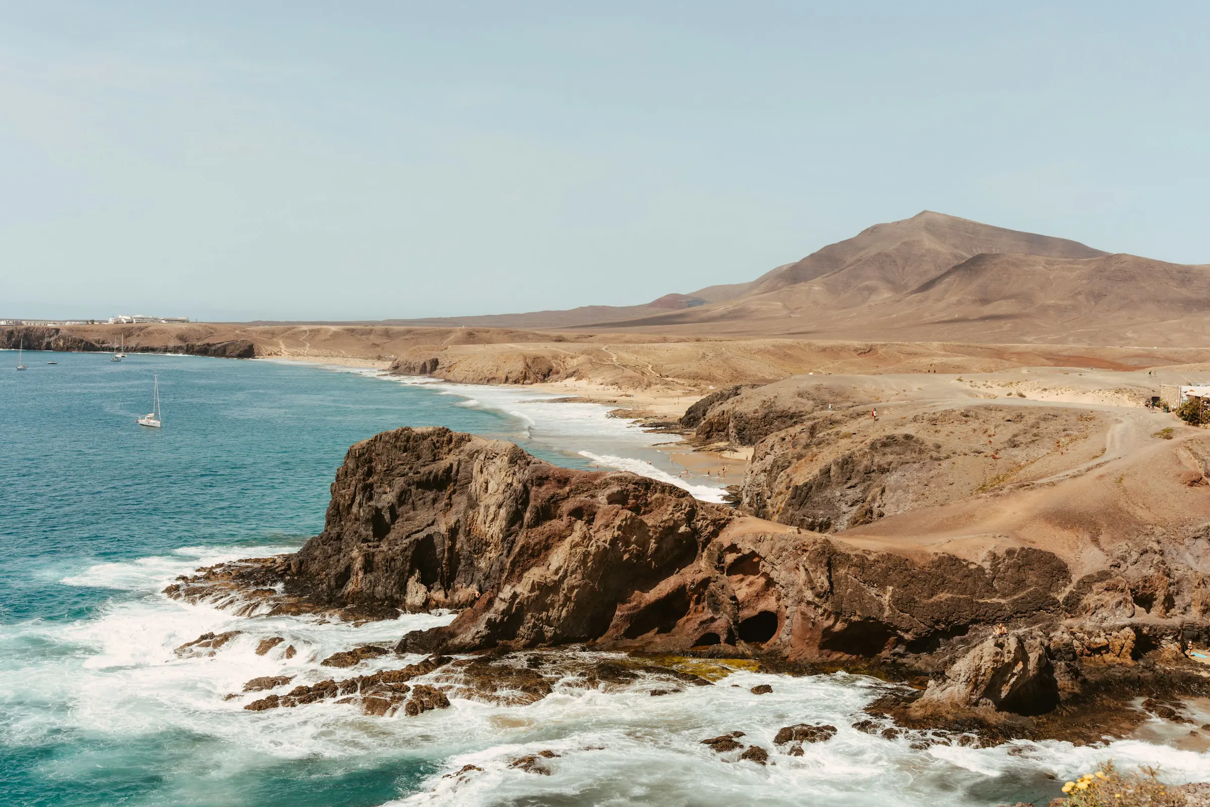 Cliff meets blue sea with waves on the coast of the Canary Islands with mountains in the background