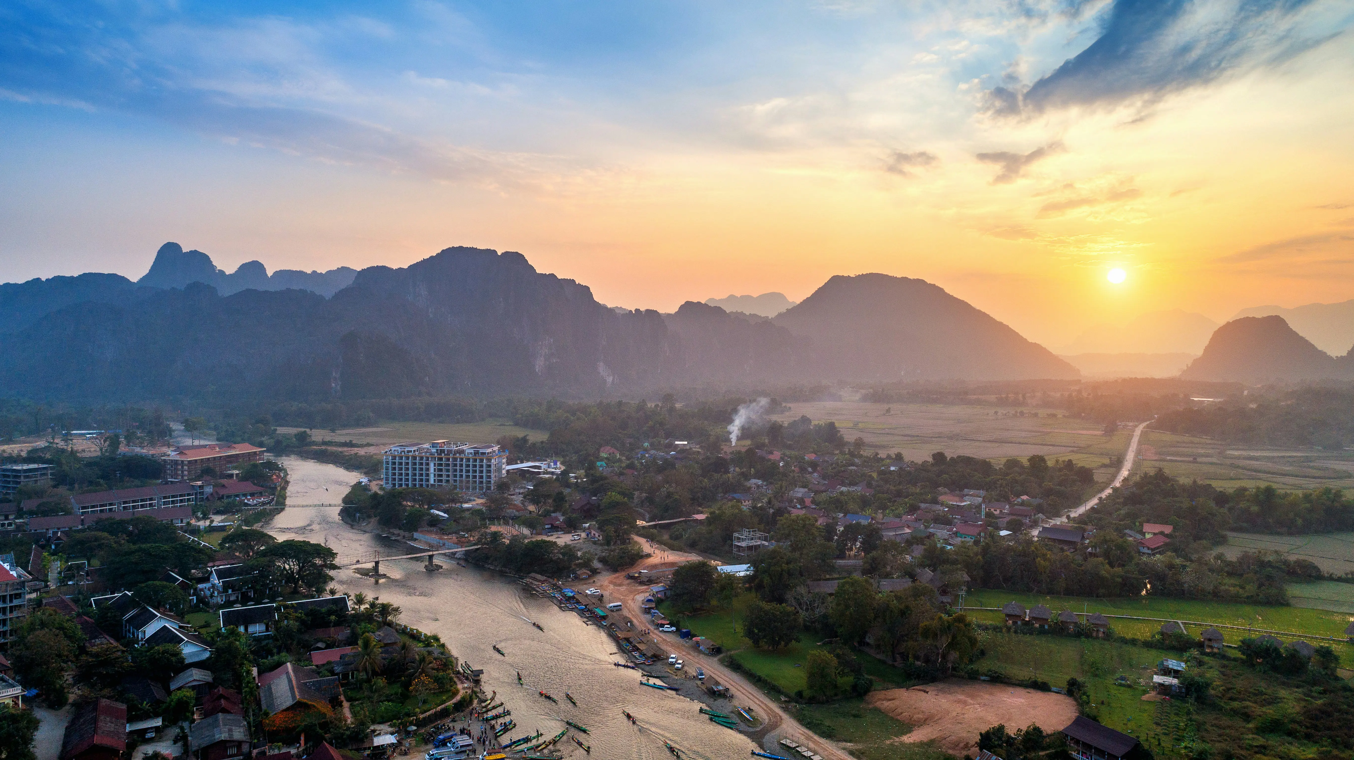 Scenic aerial view of a vibrant sunset over a picturesque valley with a river, lush greenery, and distant mountains, showcasing the tranquility and natural beauty of the landscape