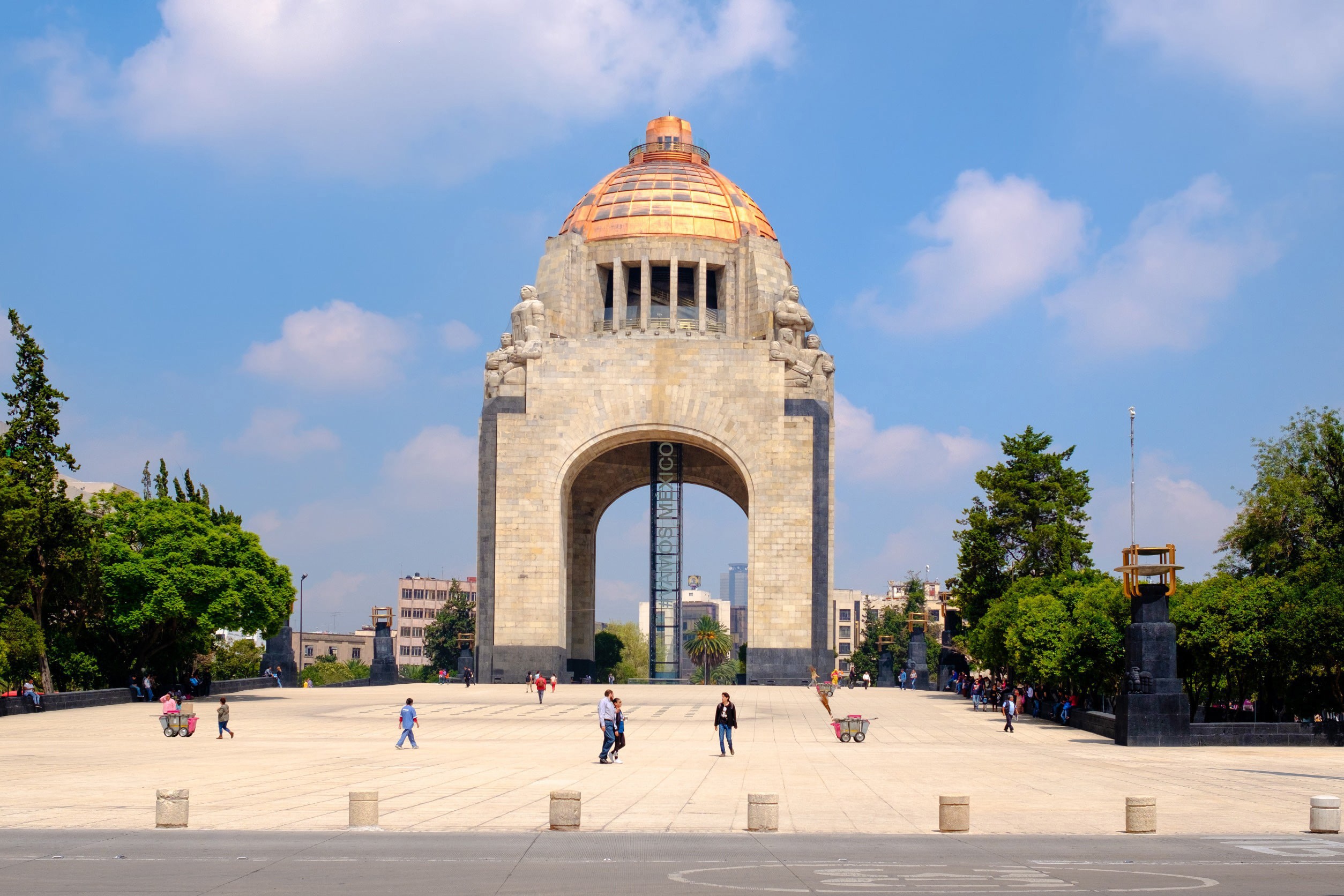 Et torg som fører opp til monumenter i Mexico City med grønne trær rundt og blå himmel i bakgrunnen