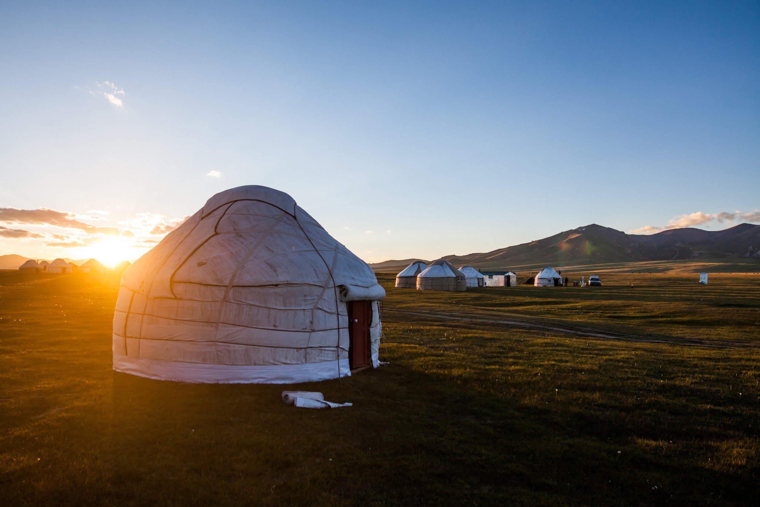 Klassisk mongolsk hytte på en slette med vakker solnedgang i bakgrunnen blant fjellene