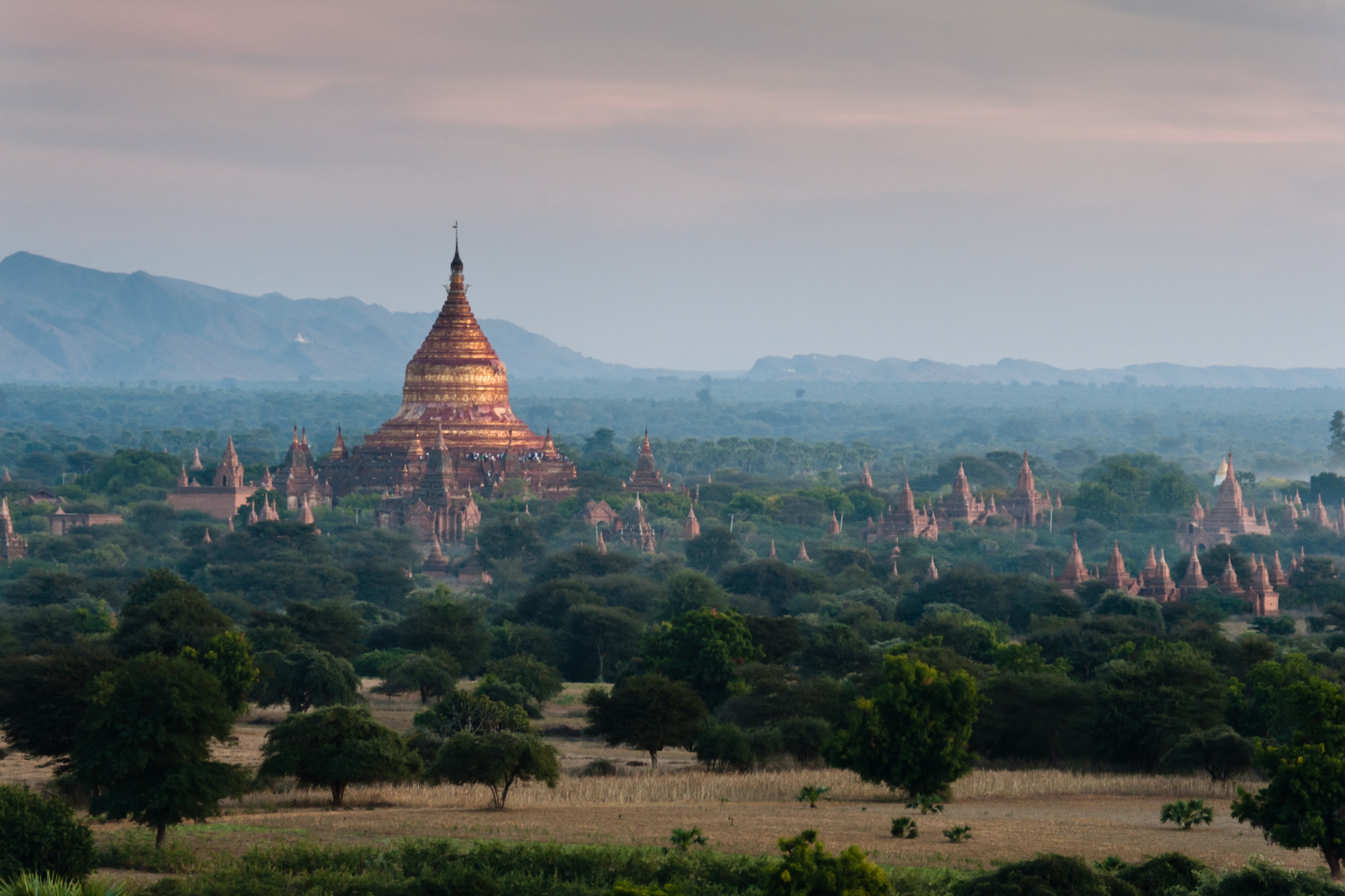 Reis til Myanmar - Vakker jungel rundt et asiatisk tempel under en solnedgang med svak tåke og klipper i bakgrunnen