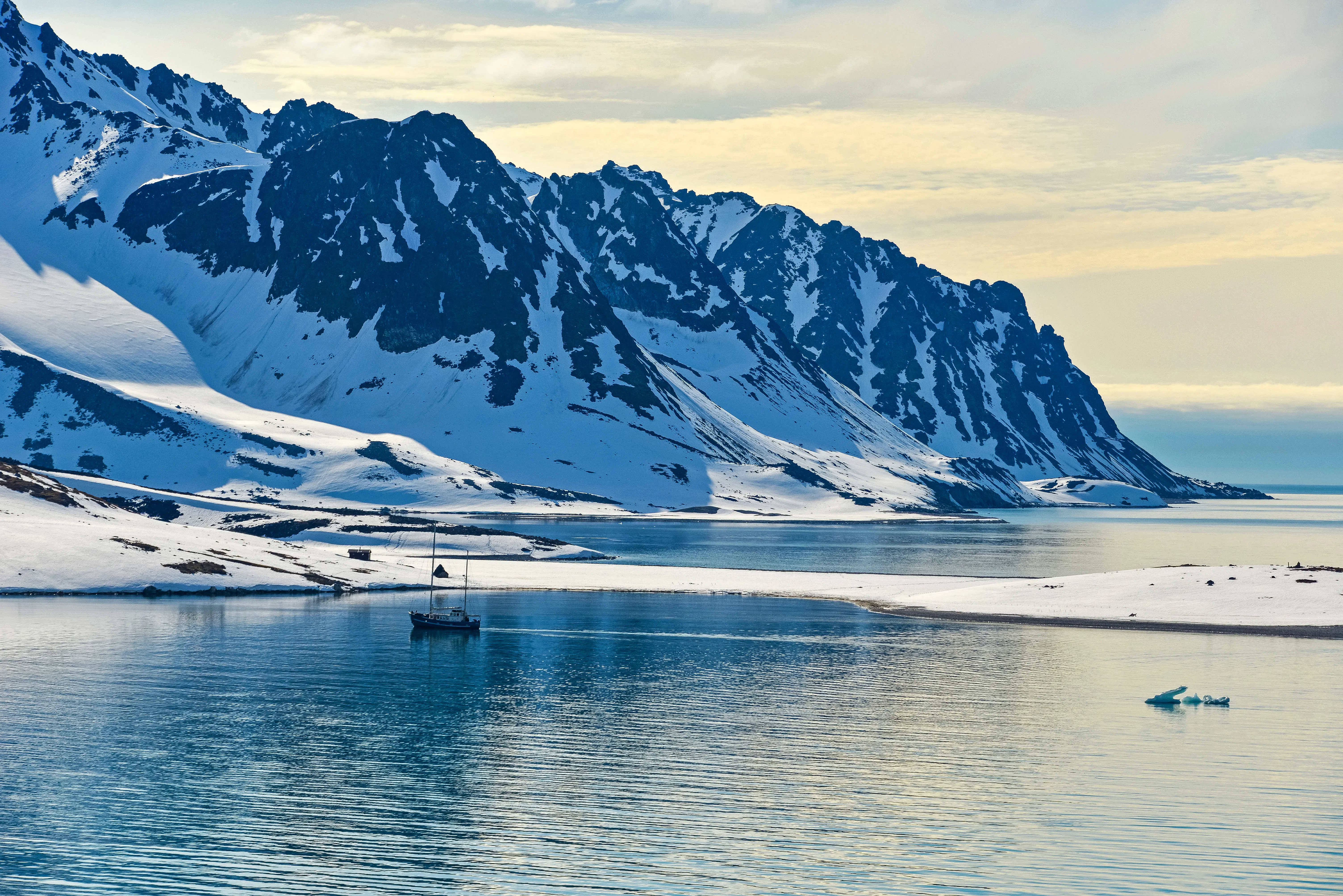 Snødekte fjell ned til isvann ved tidlig solnedgang på Svalbard