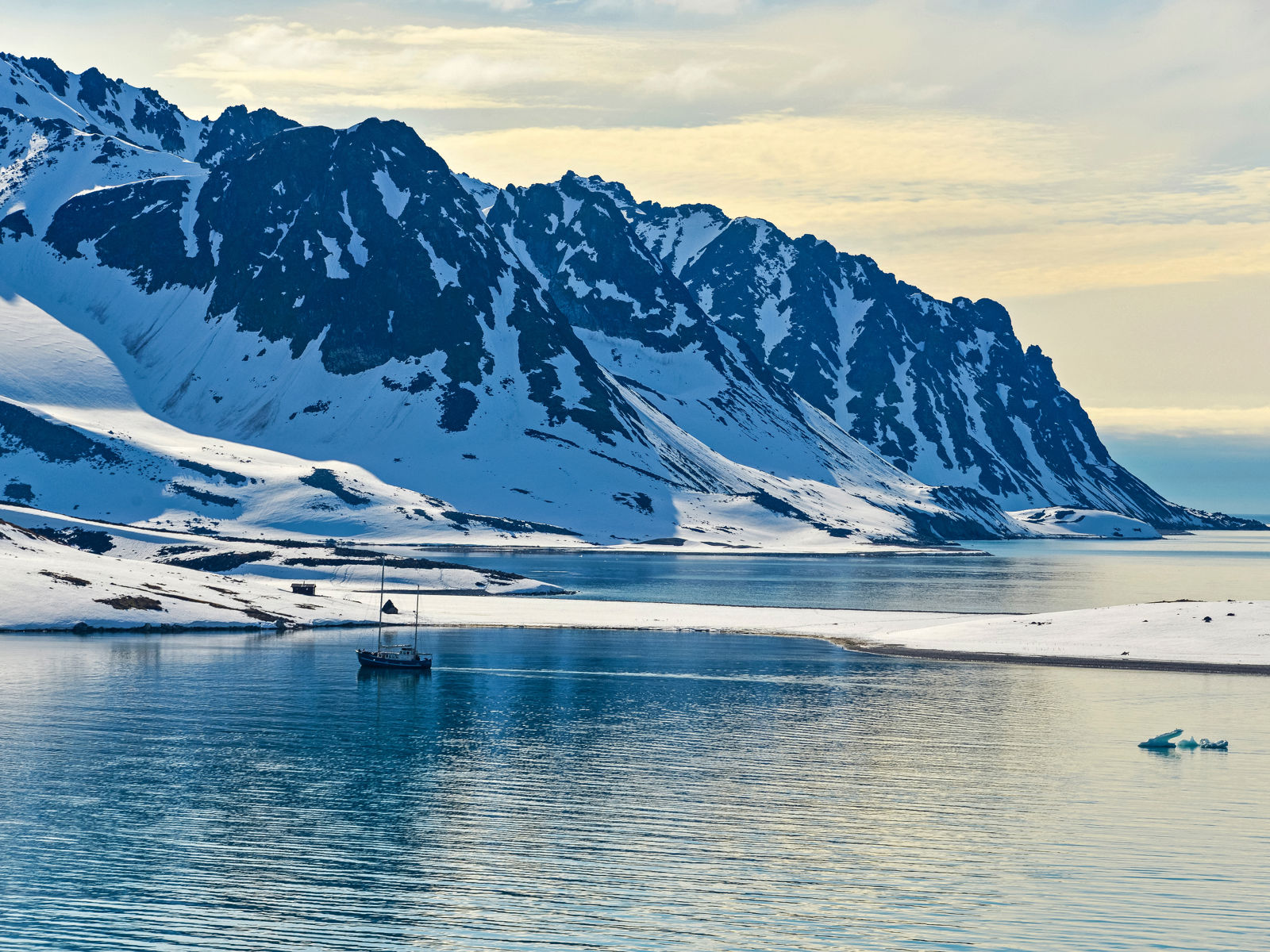 Snødekte fjell ned til isvann ved tidlig solnedgang på Svalbard