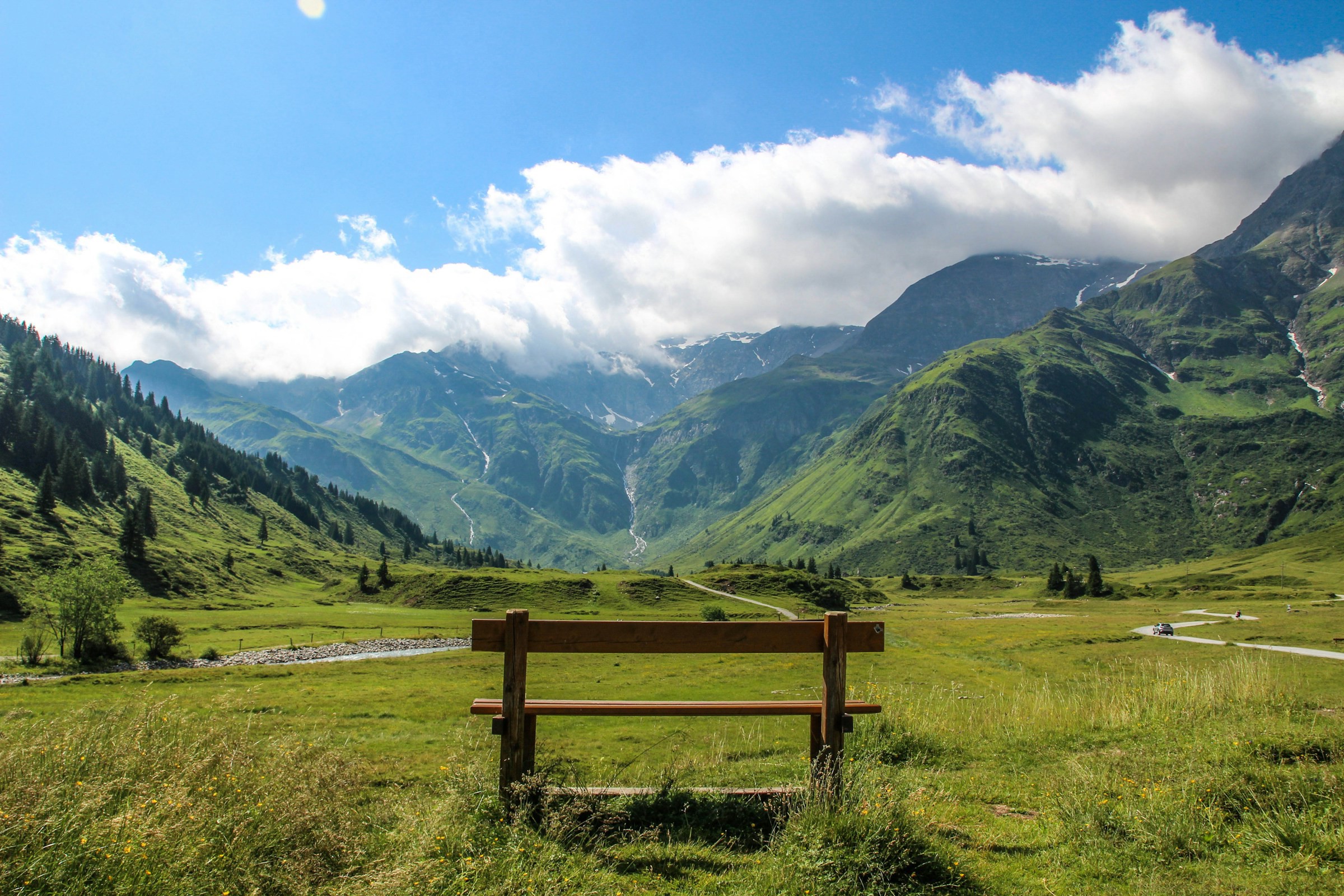 A bench on a green meadow with mountains in Austria in the background against a blue sky