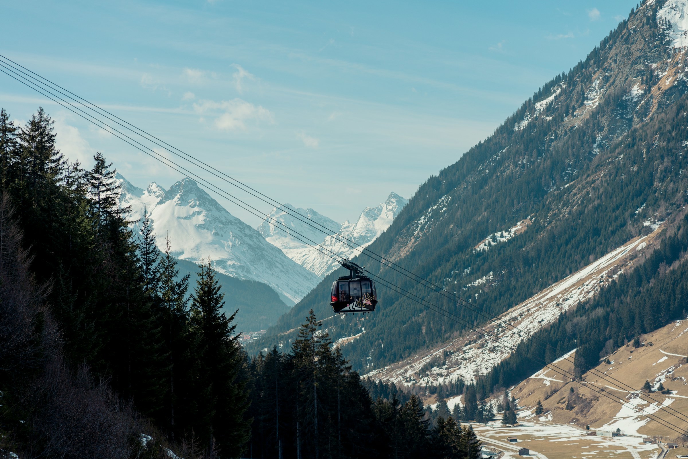 Funicular over alpine valley with snow-capped mountain peaks and pine forest in the foreground in Ischgl.