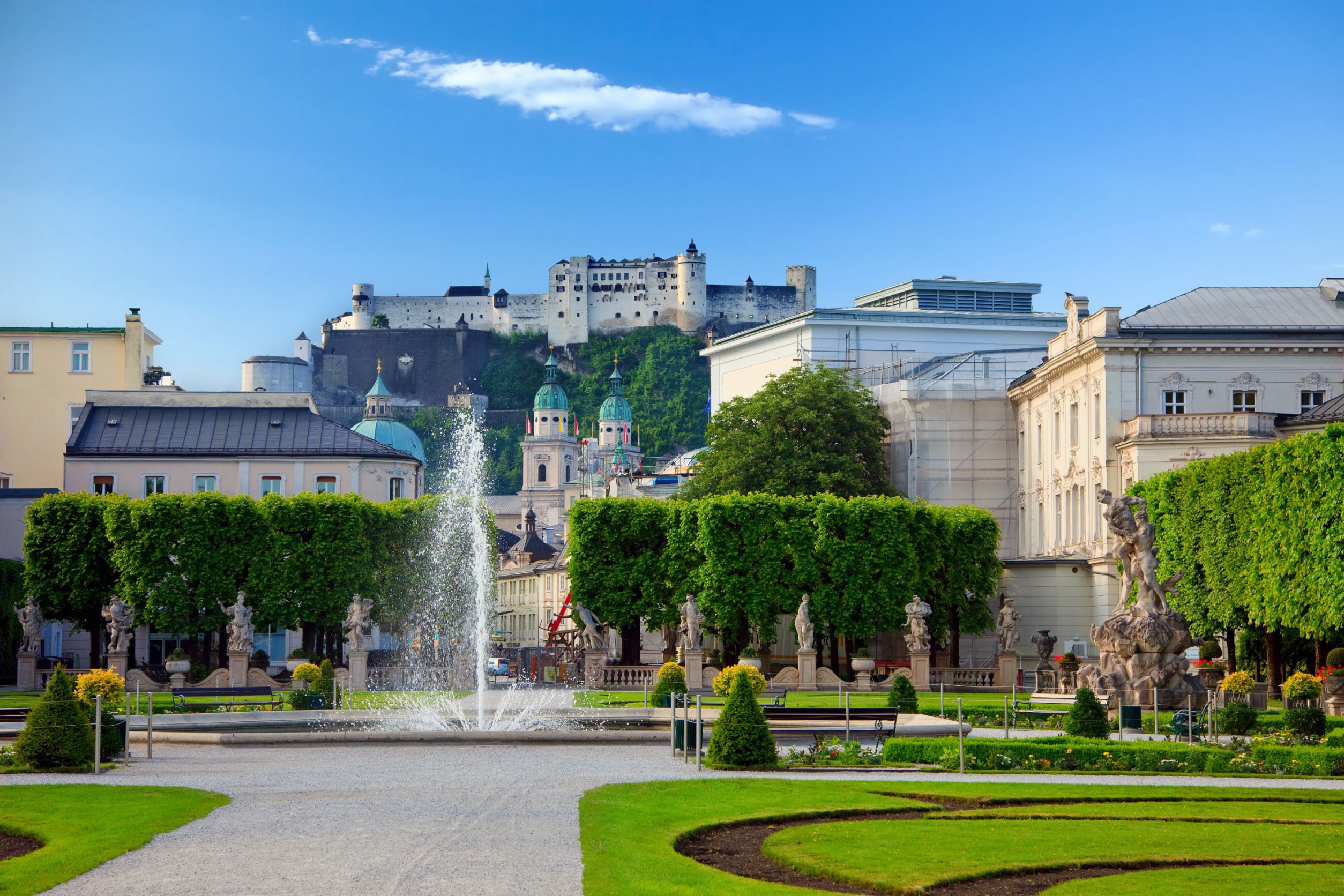 Beautiful green park with traditional European buildings and fountain against a blue sky in Salzburg