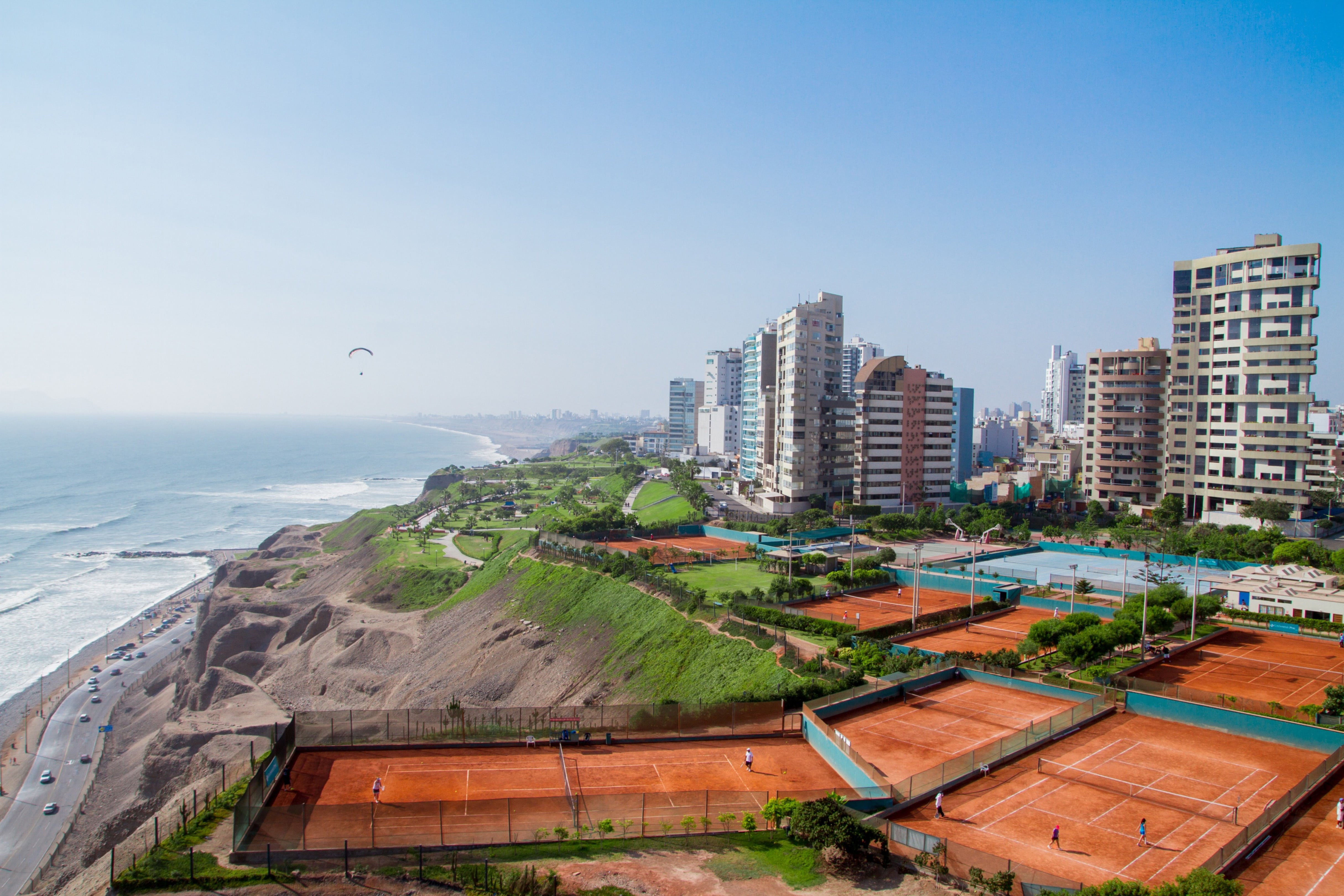 Reis til Lima - Vu over kysten der havet møter bykanten av Lima i Peru med bygninger, tennisbane og blå himmel