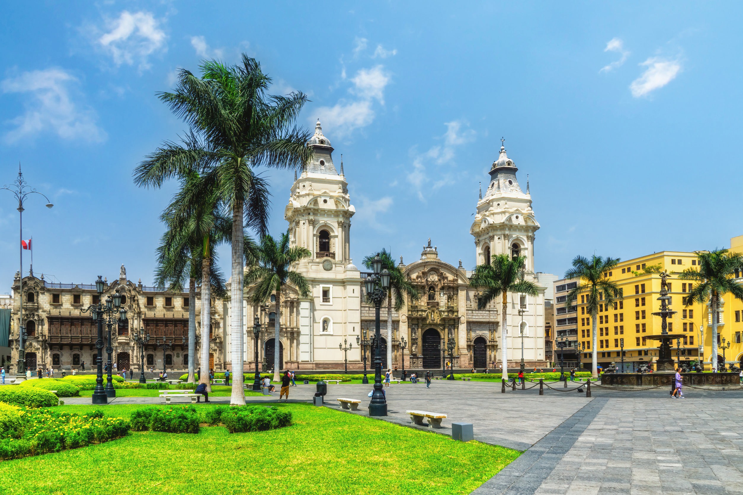 Vakkert torg med grønt gress, palmer og tradisjonelle spanske bygninger i hvitt og gult i Lima, Peru