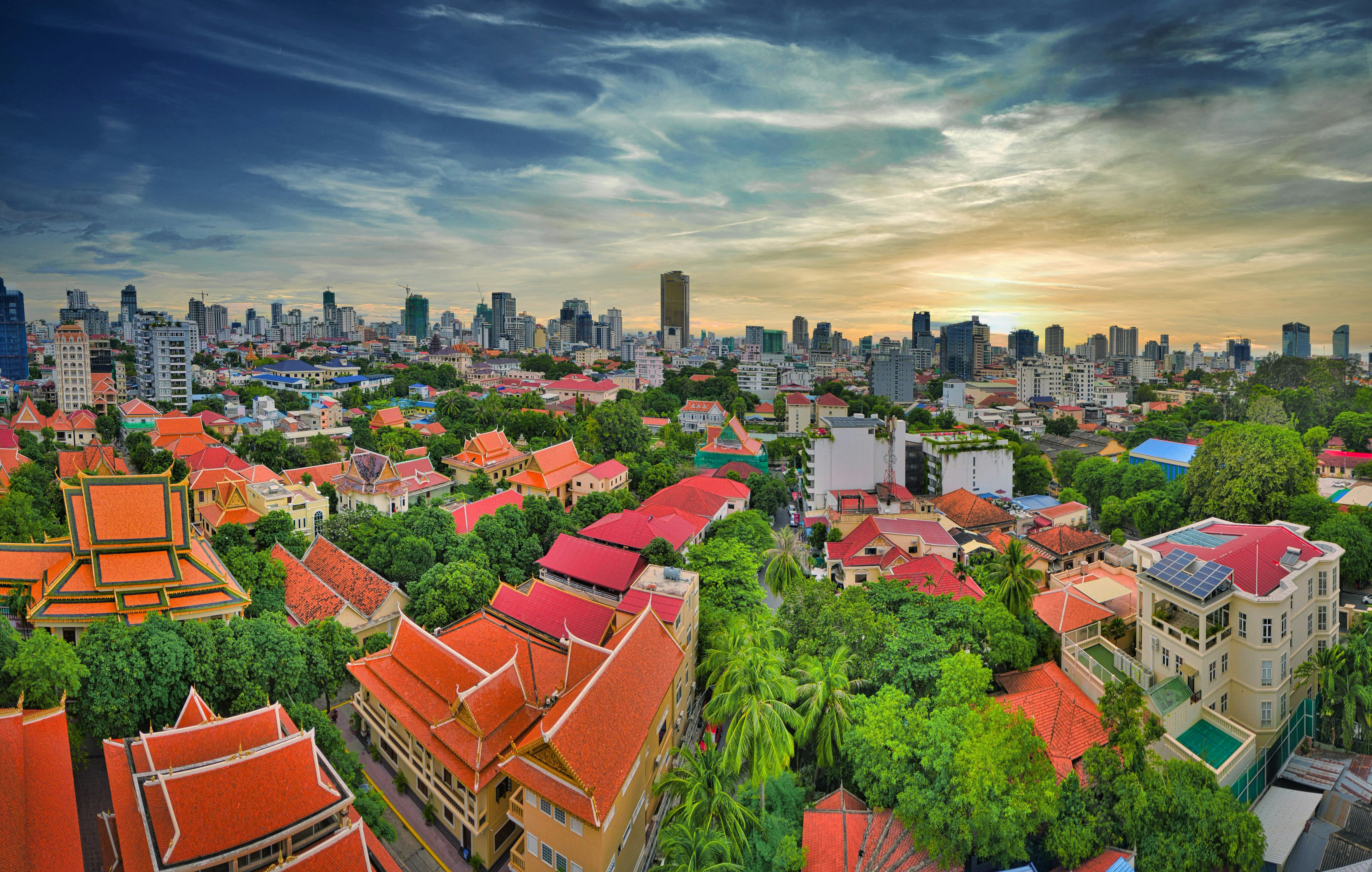 Reis til Phnom Penh - Panoramautsikt over Phnom Penh ved solnedgang med tradisjonelle og moderne bygninger omgitt av frodige trær.