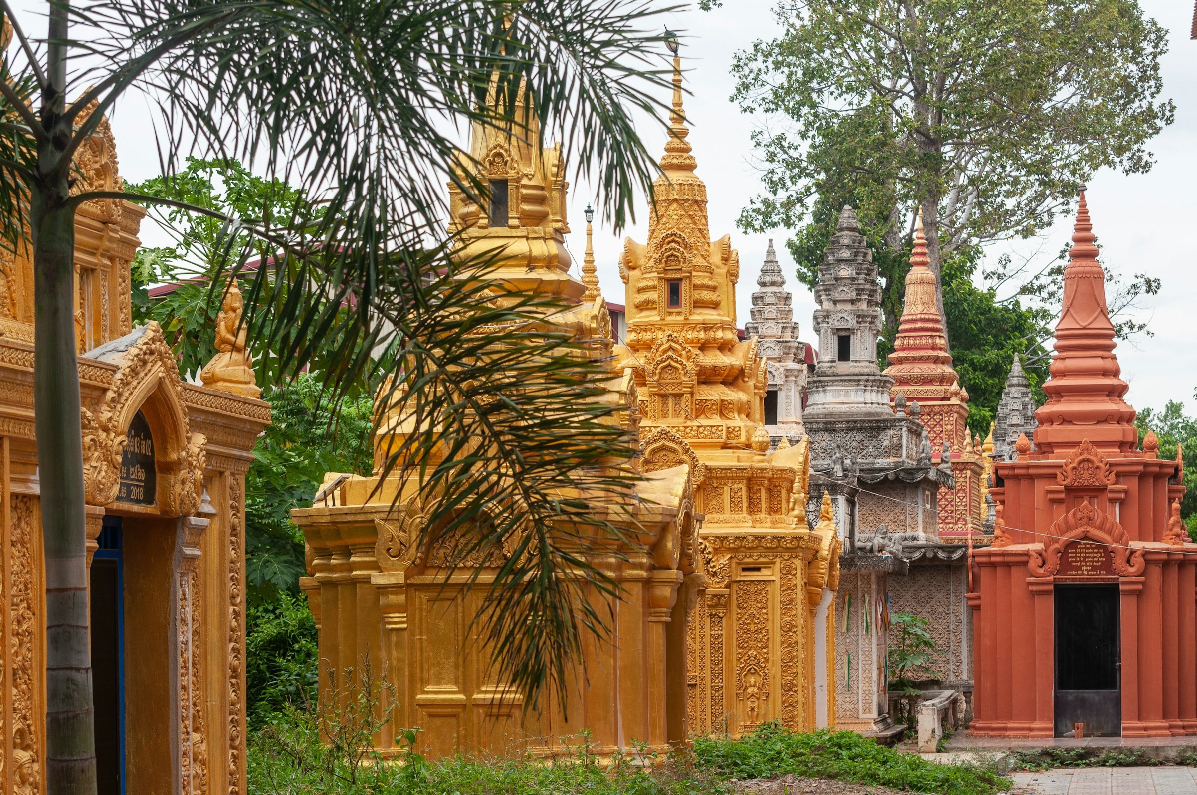 Tradisjonelle gylne og terrakotta-stupaer ved et tempel omgitt av grøntområder i Phnom Penh.