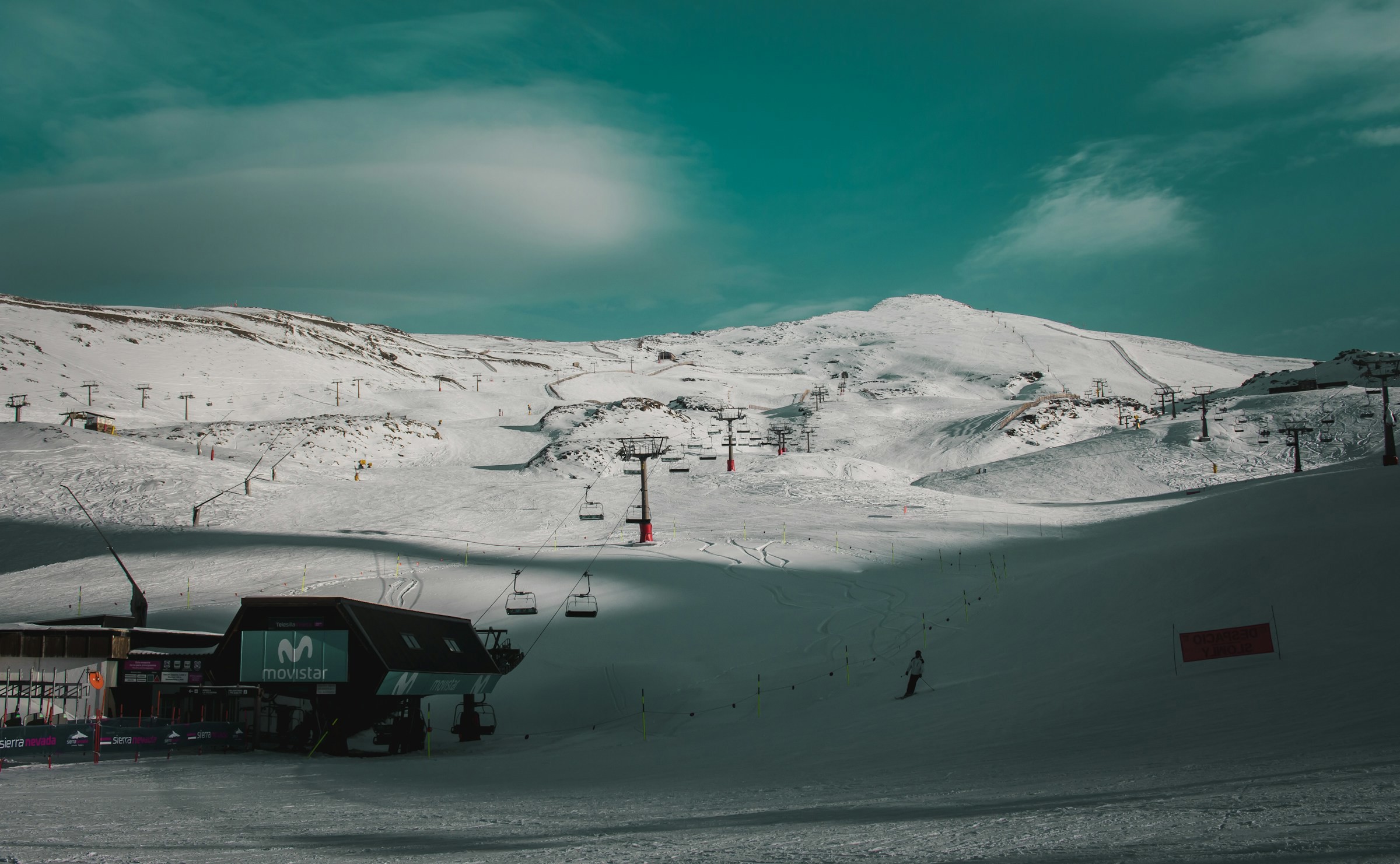 Ski slope with ski lift leads up to snow-capped mountains and dark blue skies in the Sierra Nevada