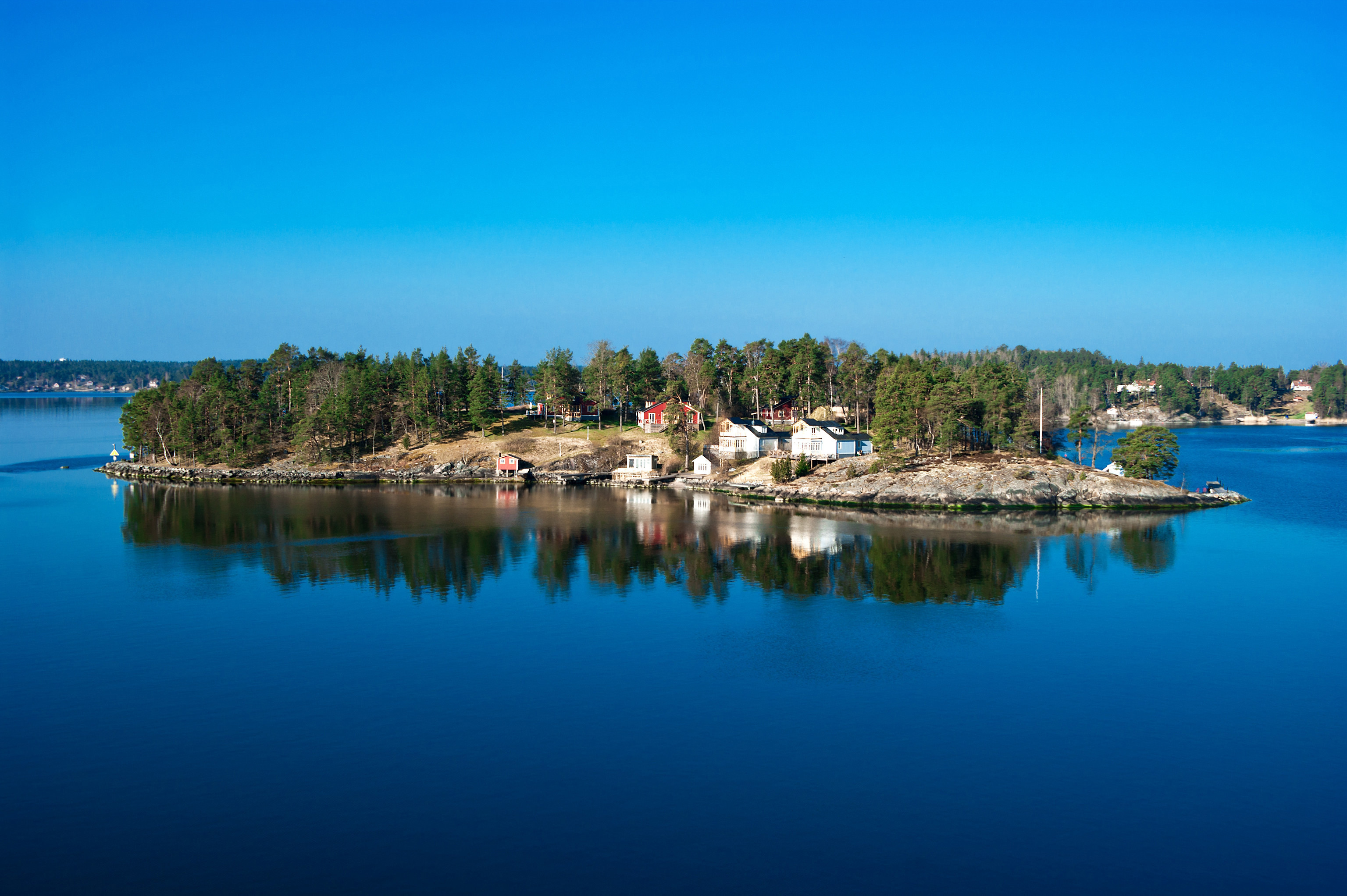 Idyllic small island with houses surrounded by calm blue waters reflecting a clear sky in Sweden.