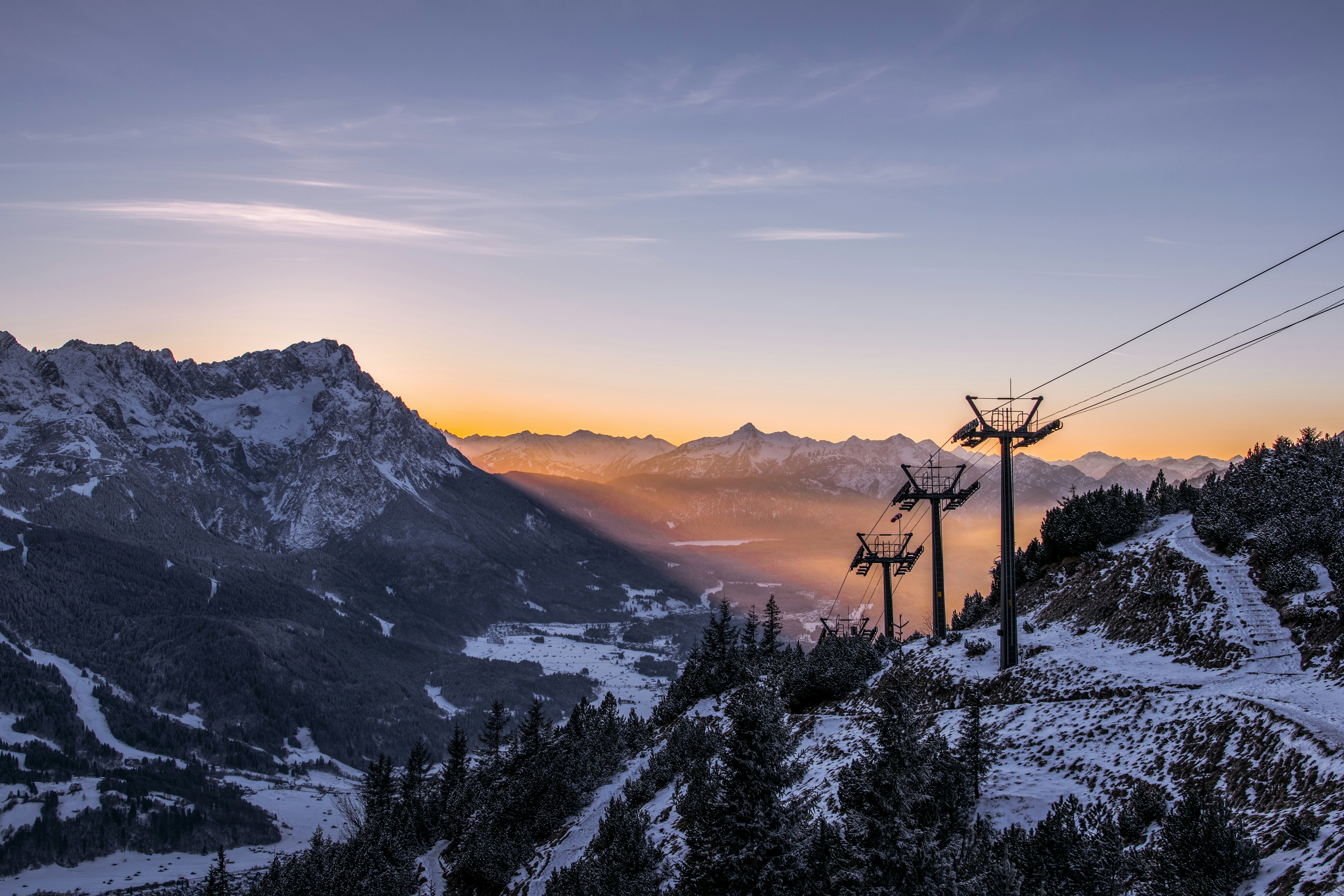 Sunset between the peaks of snow-capped mountains and a lift in the middle for skiing