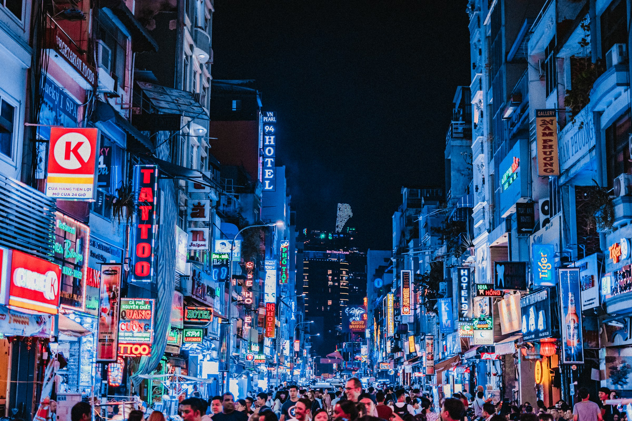Livlig bygate om kvelden i Ho Chi Minh City med neonlys og skilt, publikum spaserer i storbyatmosfære.